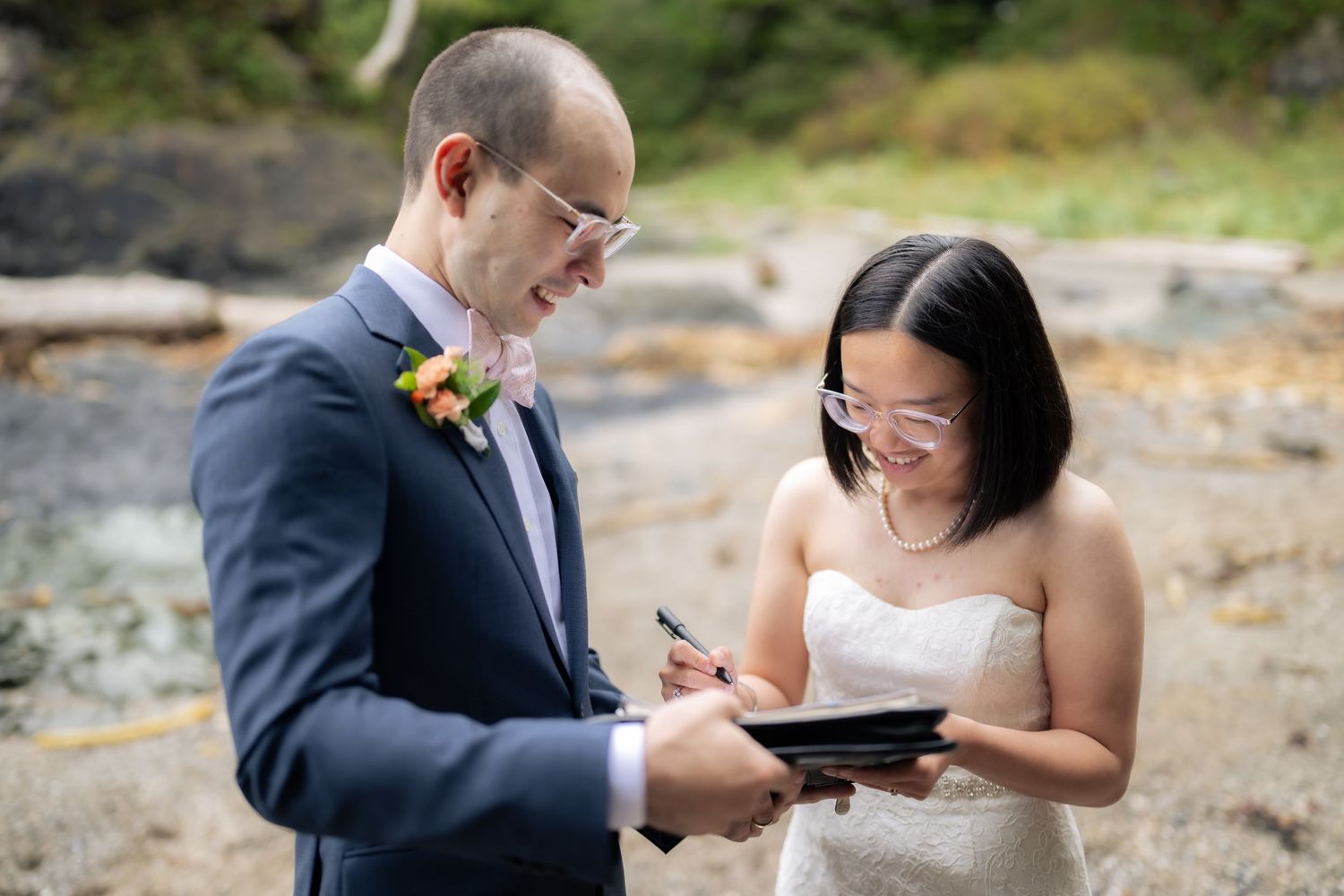 A couple shares a joyful moment while reading from small books during their outdoor wedding ceremony.