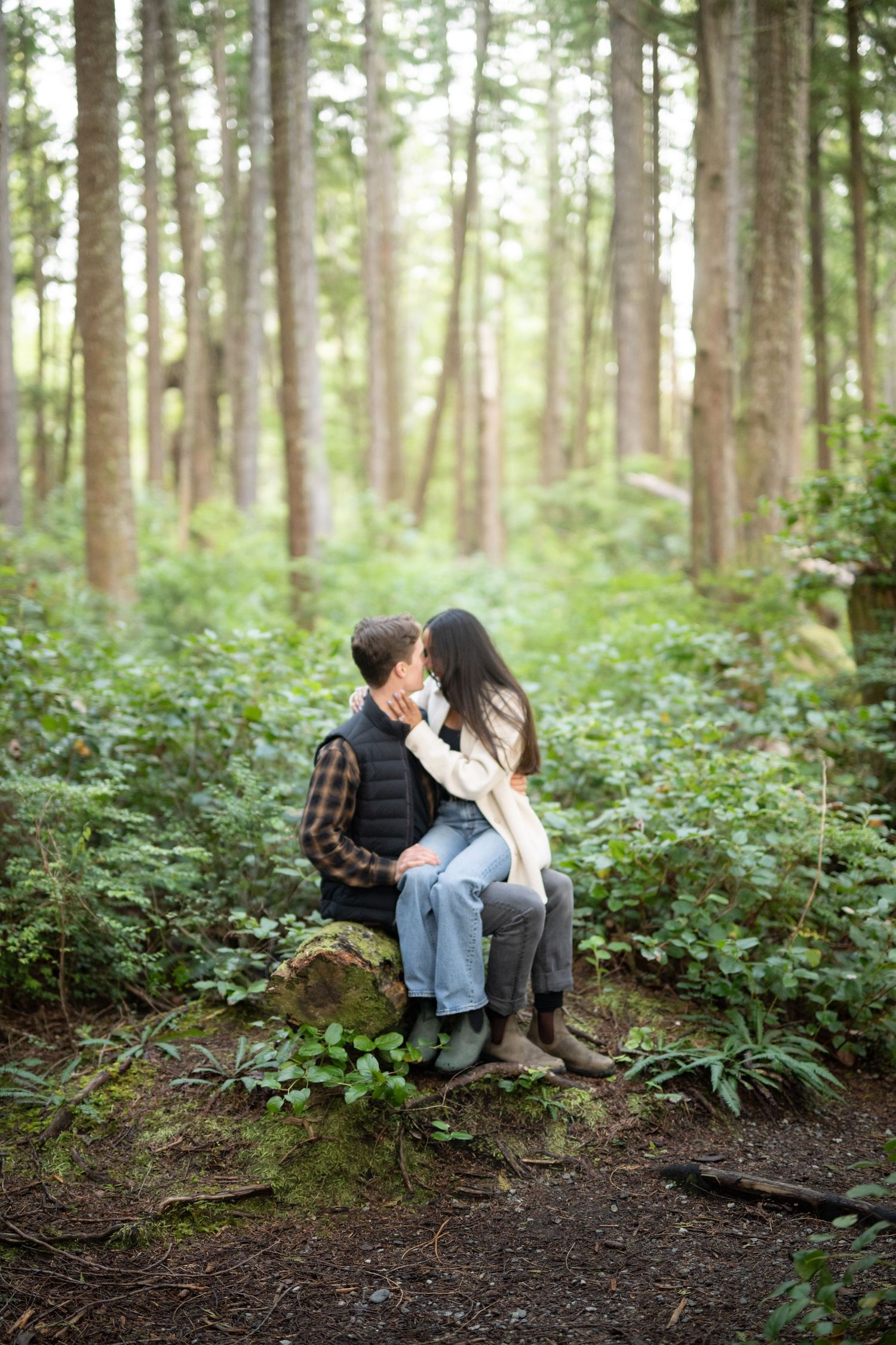Couple sharing an intimate moment while sitting on a log in a lush Pacific Northwest forest setting.