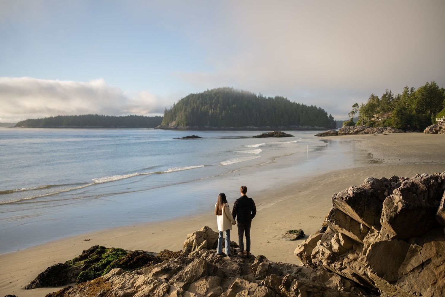 Panoramic view of a Pacific Northwest beach with forested headlands and cloudy skies.