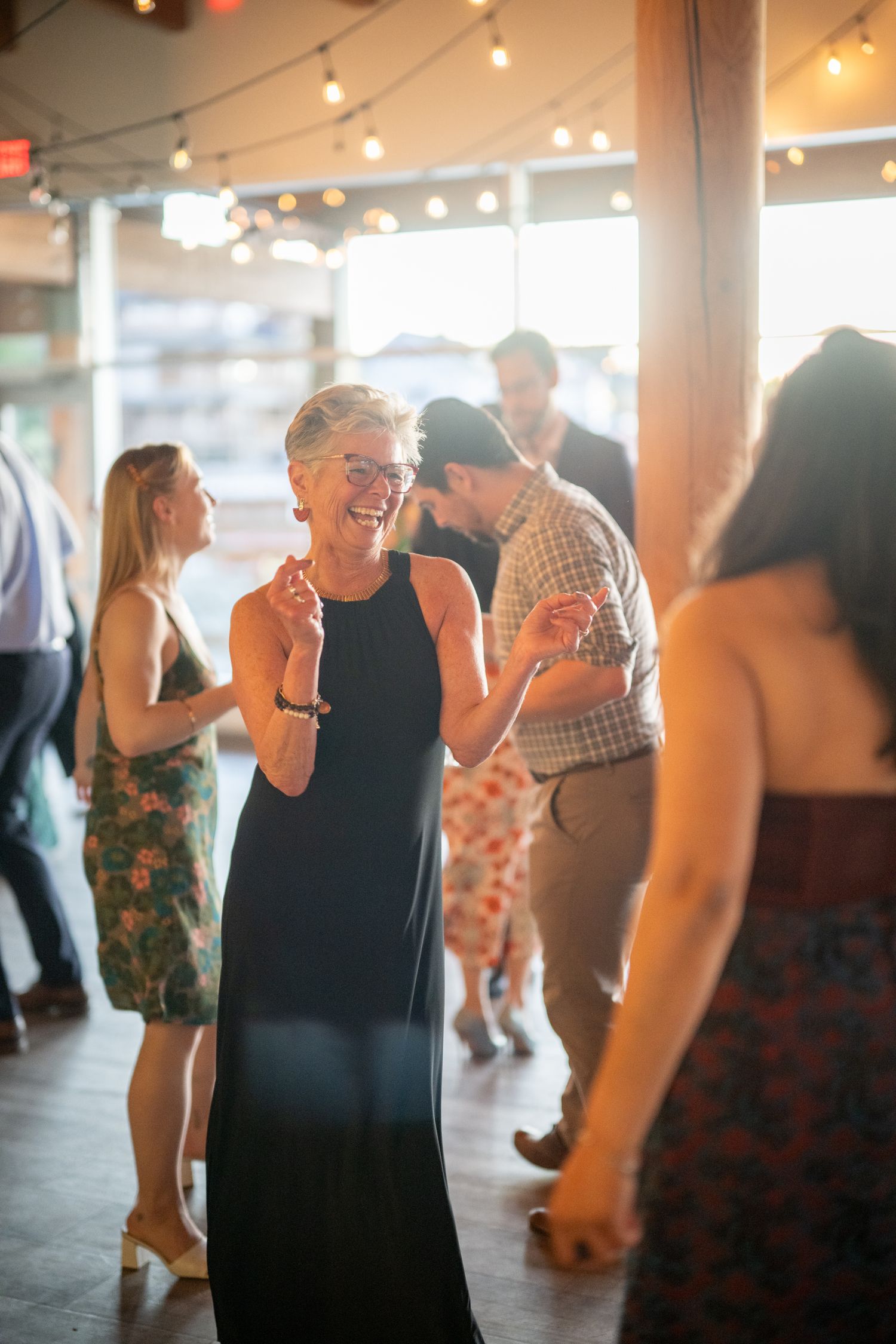 Wedding guests dancing in a spacious venue with ambient lighting and exposed wooden beams.