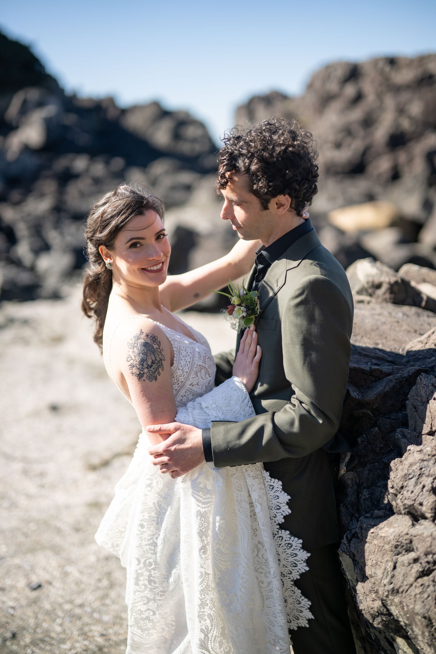 Romantic wedding couple embracing among rocky coastal scenery.