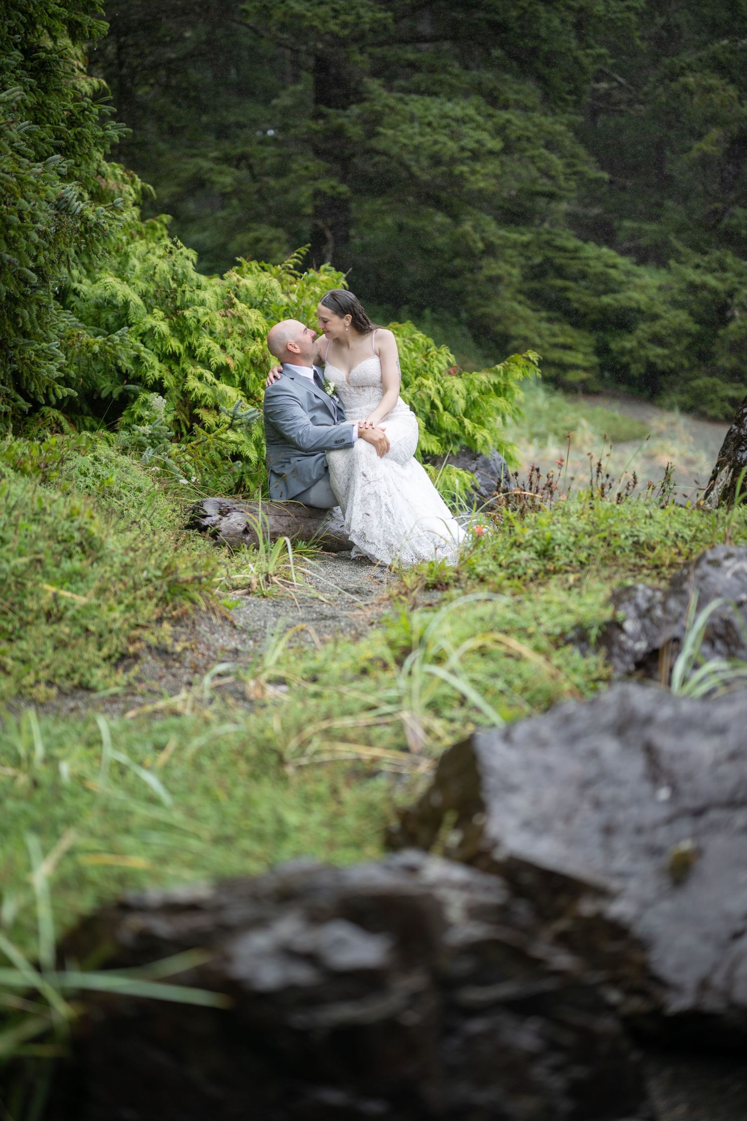 Wedding couple embraces on a rocky cliff surrounded by green forest.