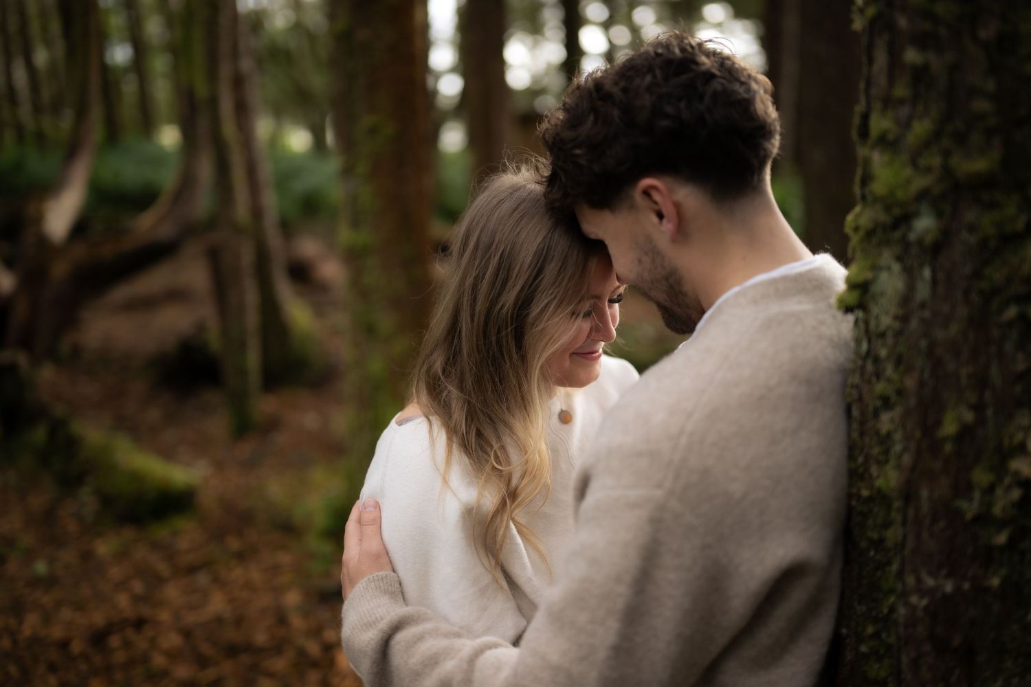 A series of intimate forest portraits showing gentle moments between two people in neutral clothing.