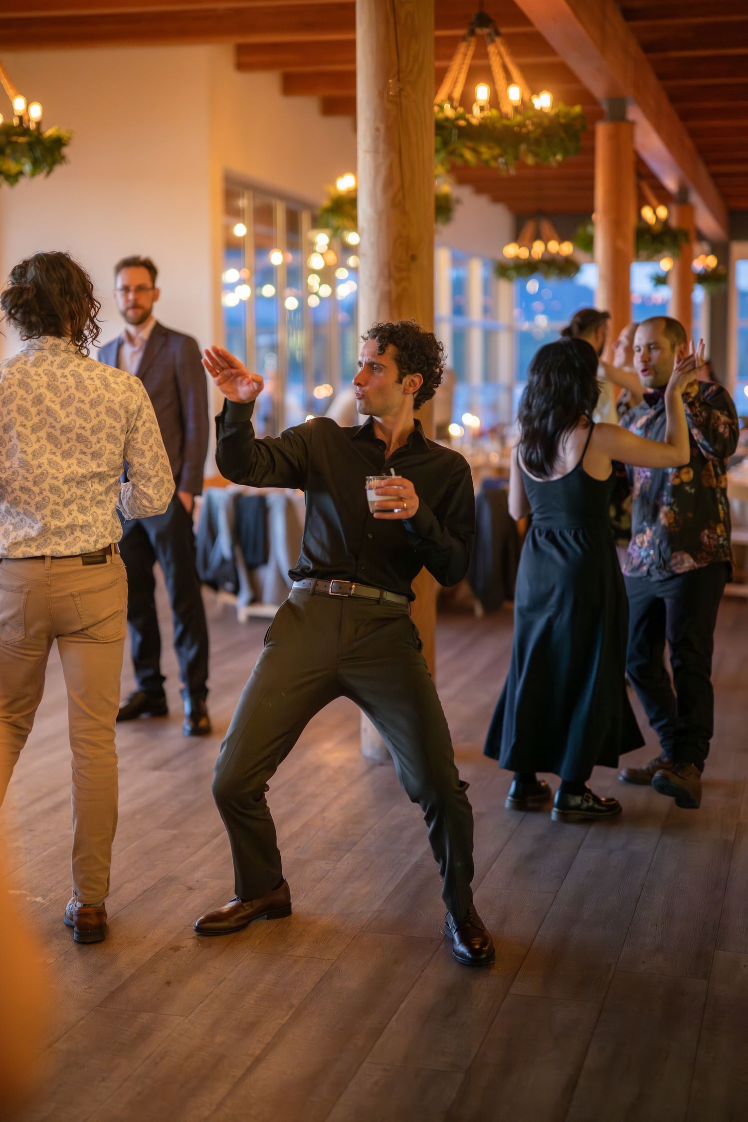 Wedding guests dancing on a wooden floor under chandeliers in a rustic venue.
