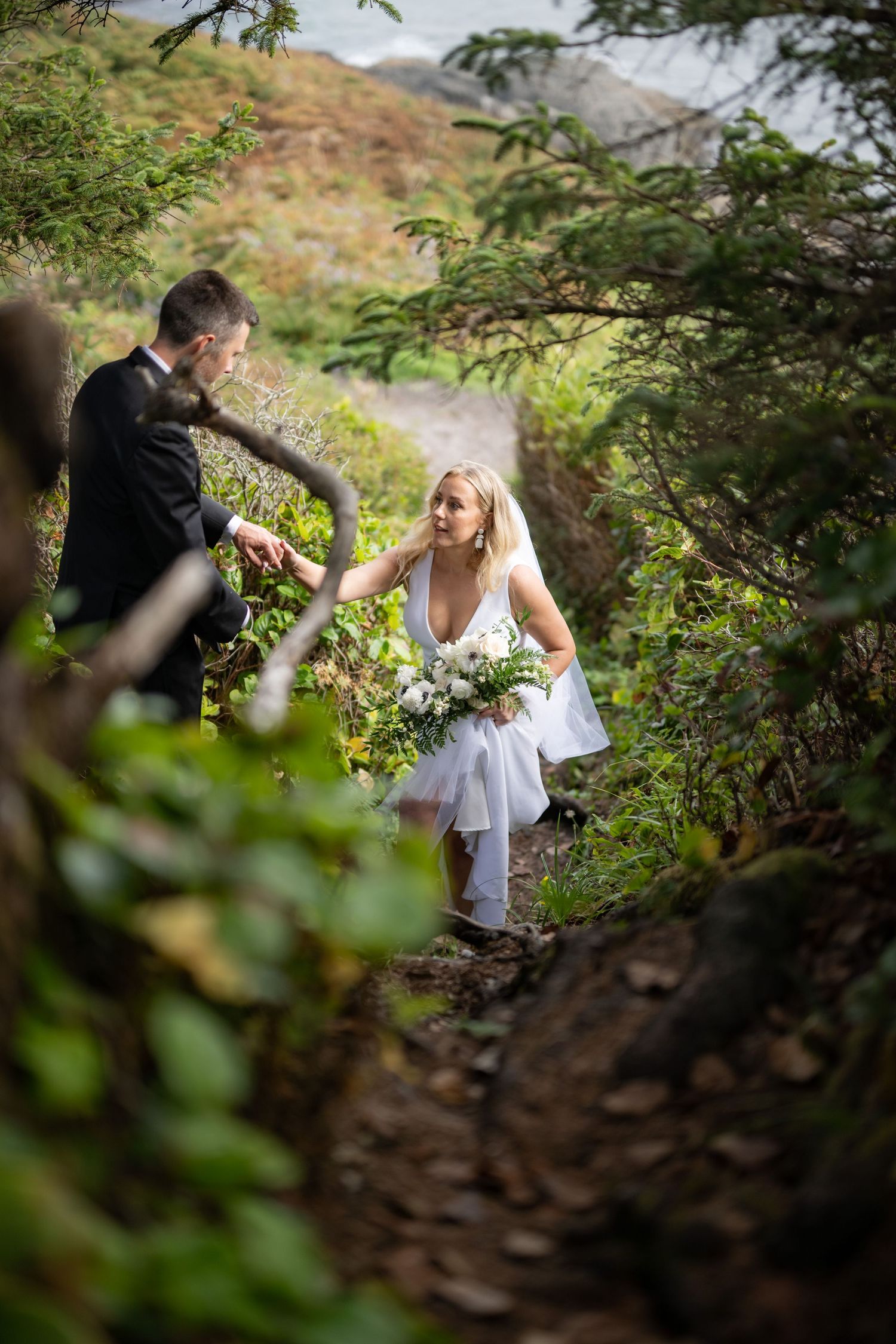 A couple walking through lush forest vegetation on a mountain trail.