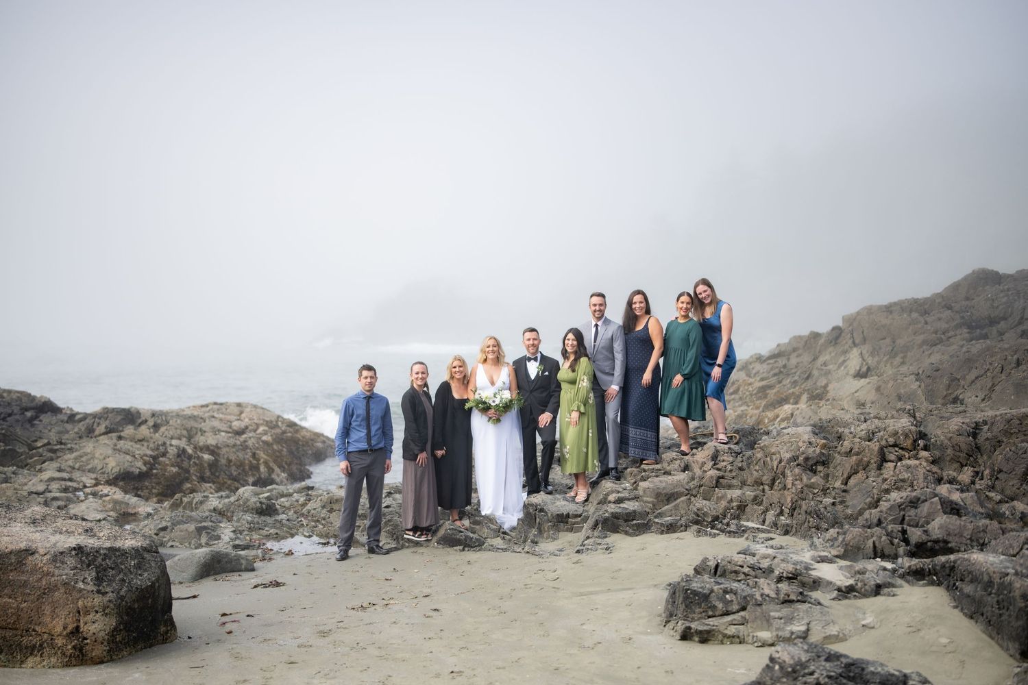Group photo of wedding guests gathered on rugged oceanside cliffs.