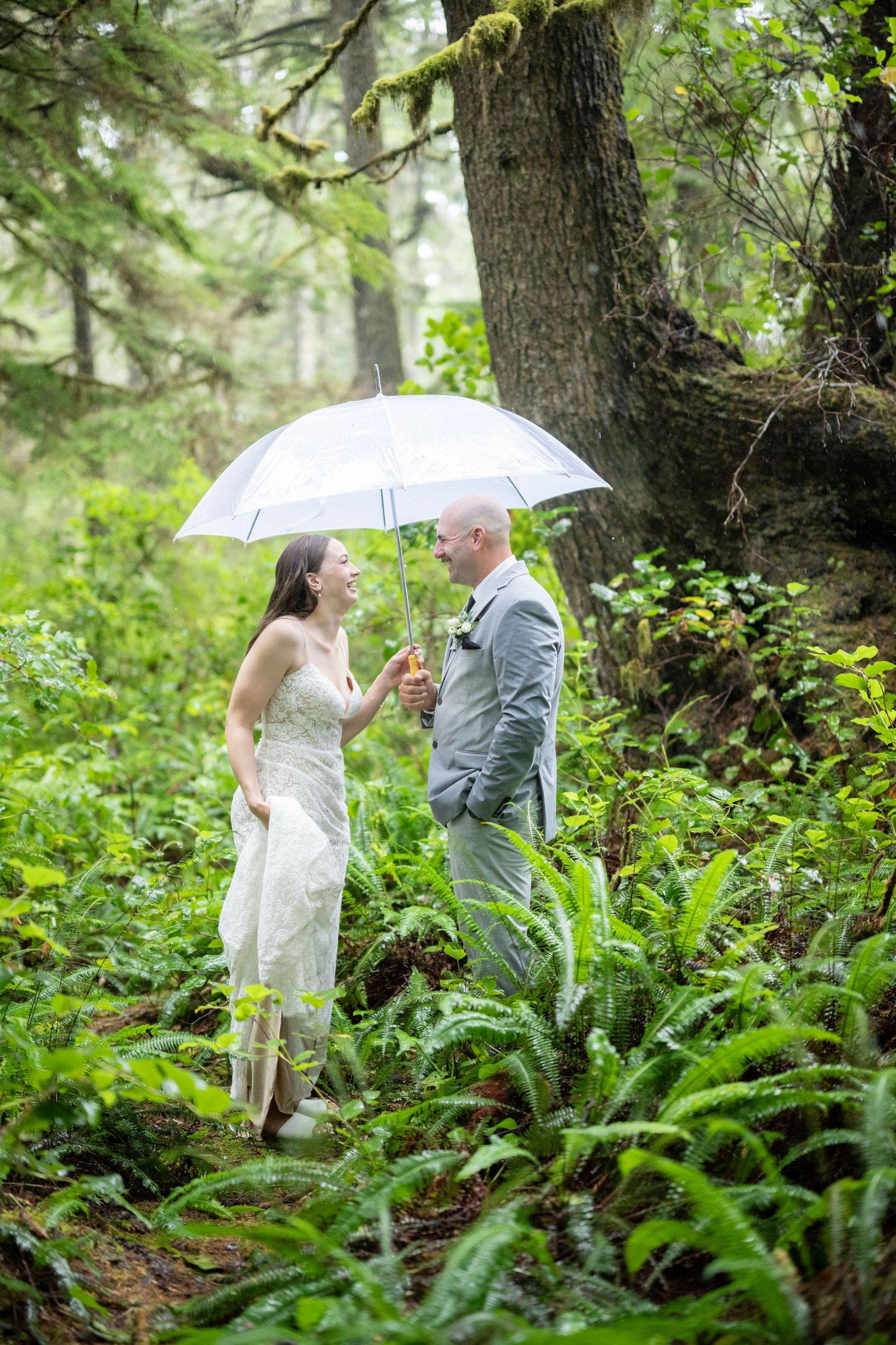 Couple sharing an intimate moment under a white umbrella in a verdant forest setting.