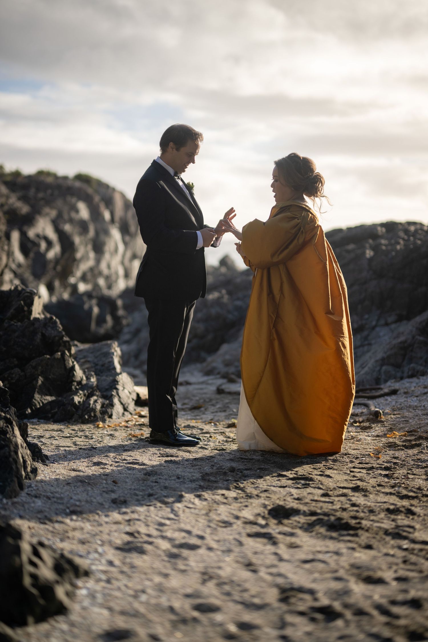 A couple shares an intimate moment on rocky beach cliffs during sunset.