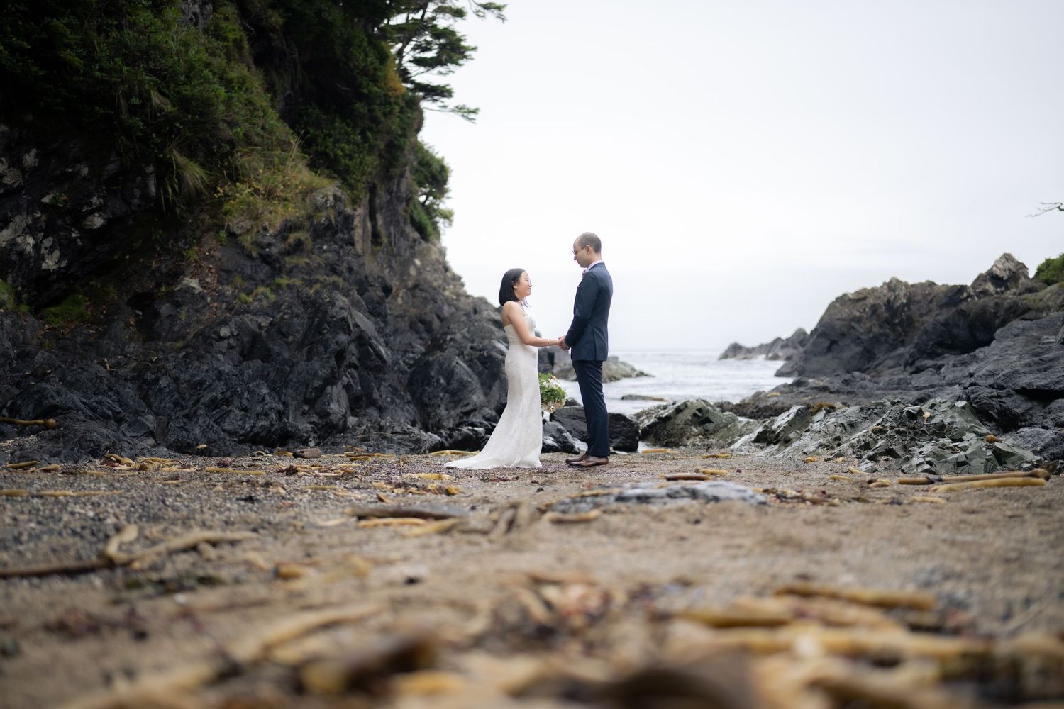 Intimate beach wedding ceremony with rocky cliffs and evergreen trees in the background.