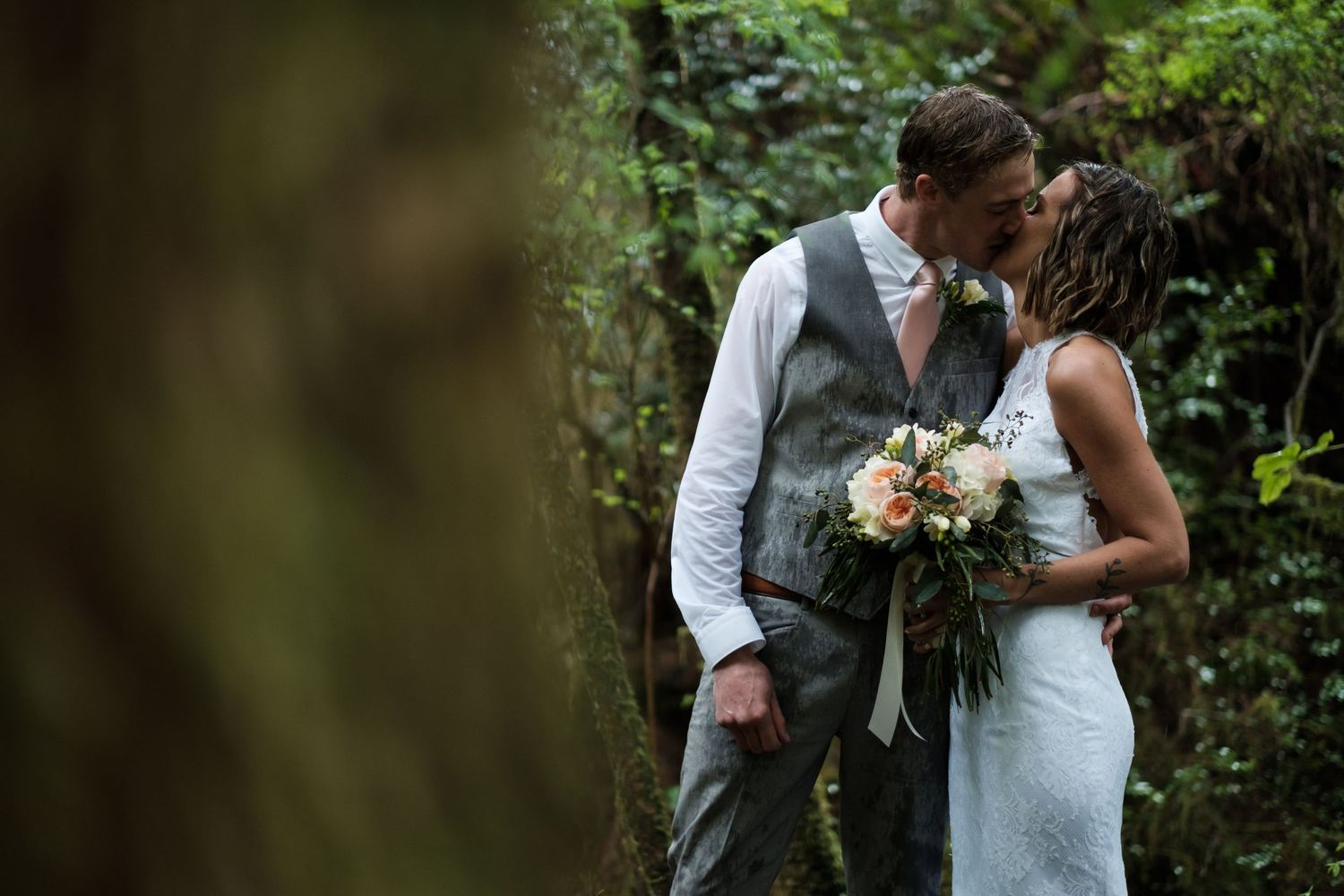 A couple shares an intimate moment in a lush forest setting.