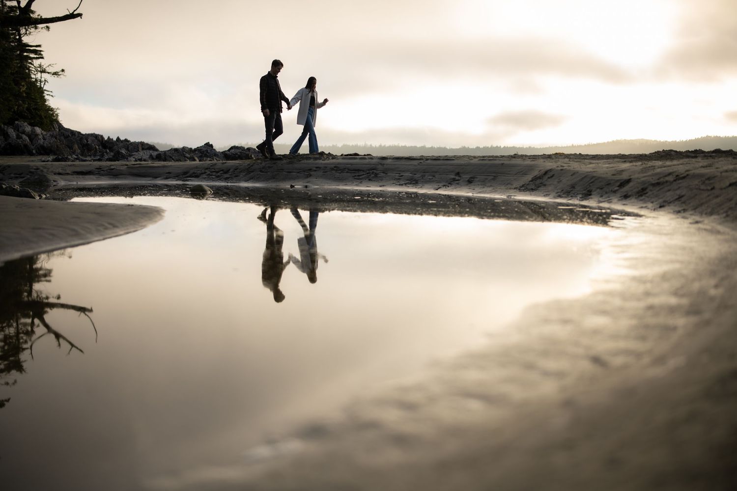 Reflective beach scene with silhouettes walking along the shoreline at sunset.