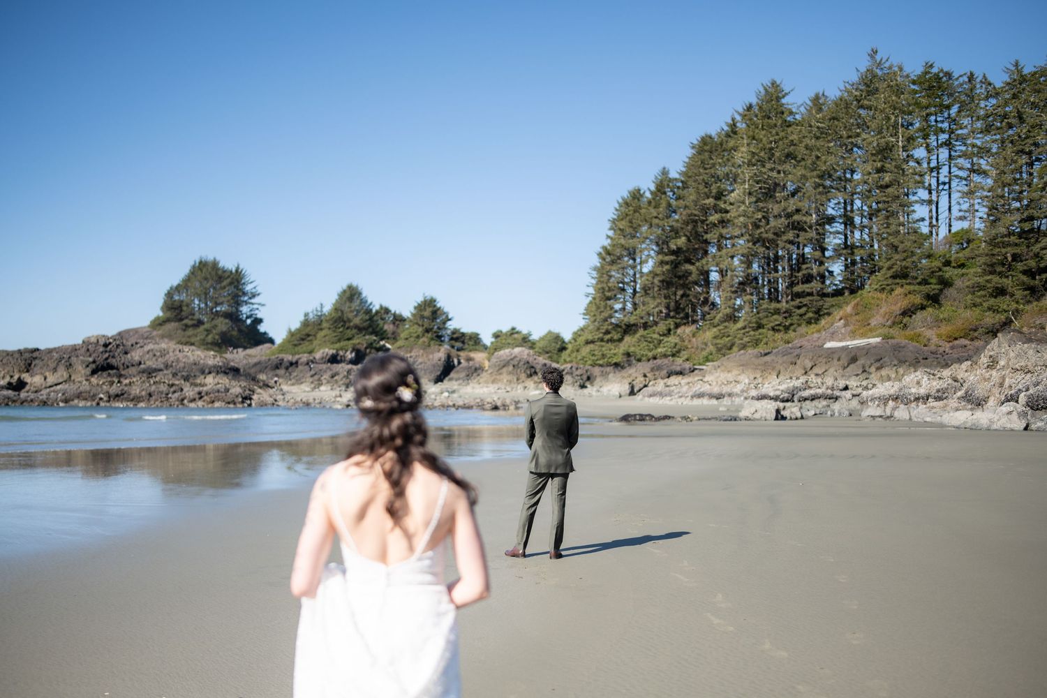 A beach wedding scene with evergreen trees and rocky coastline in the background.