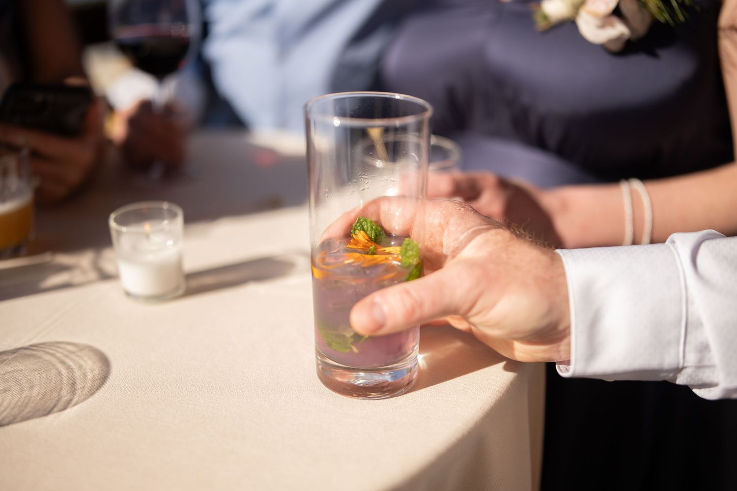Hand holding a garnished cocktail in a tall glass during an event.