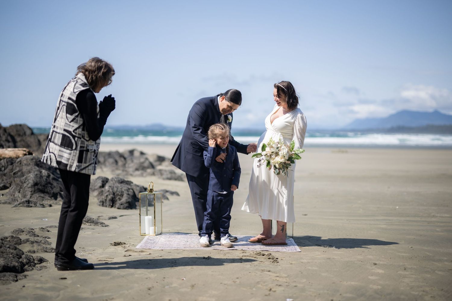 A small wedding gathering on a sandy beach with rocky cliffs and ocean views.