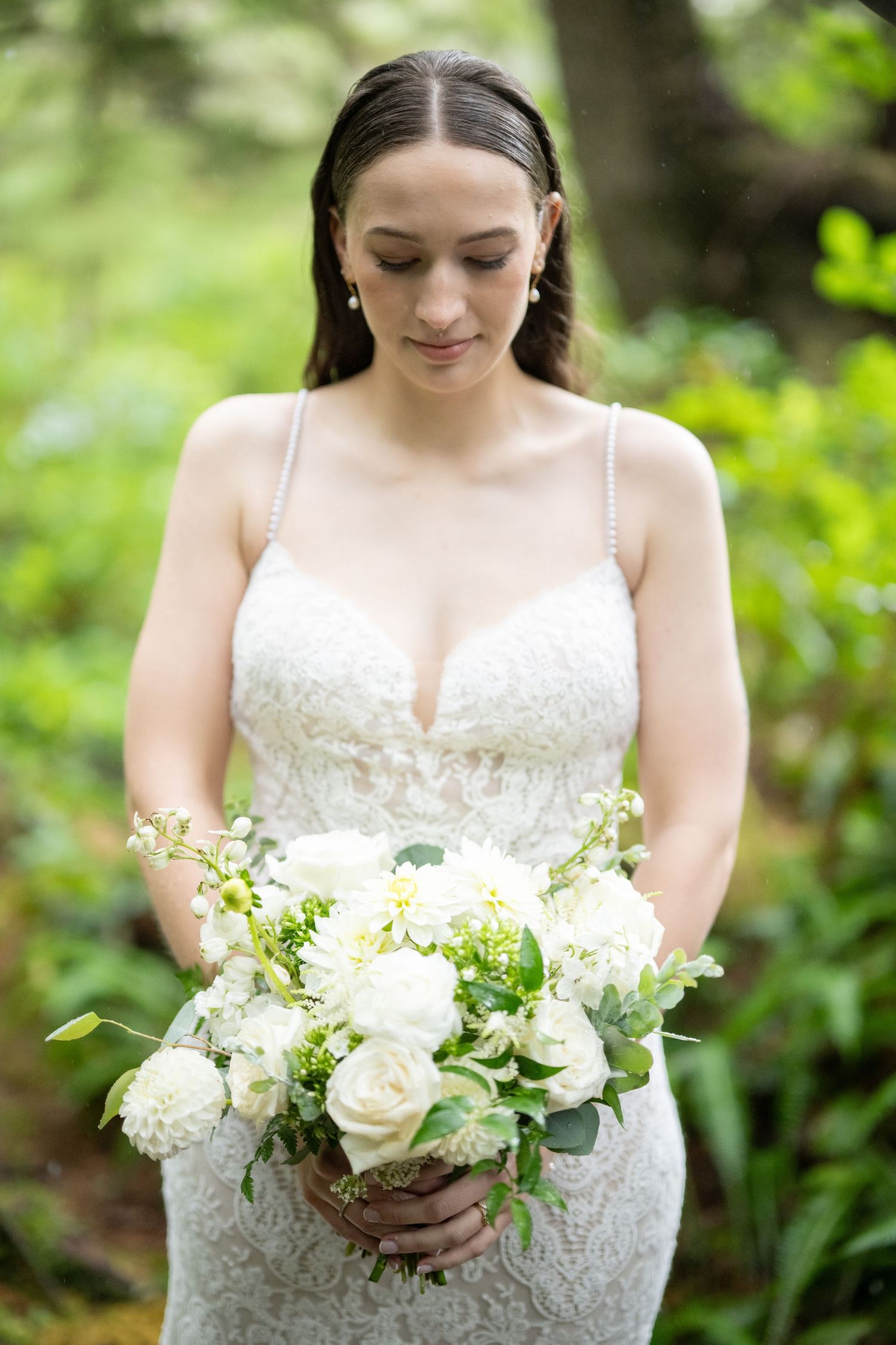A bridal bouquet of white roses and greenery held against a lace wedding dress.