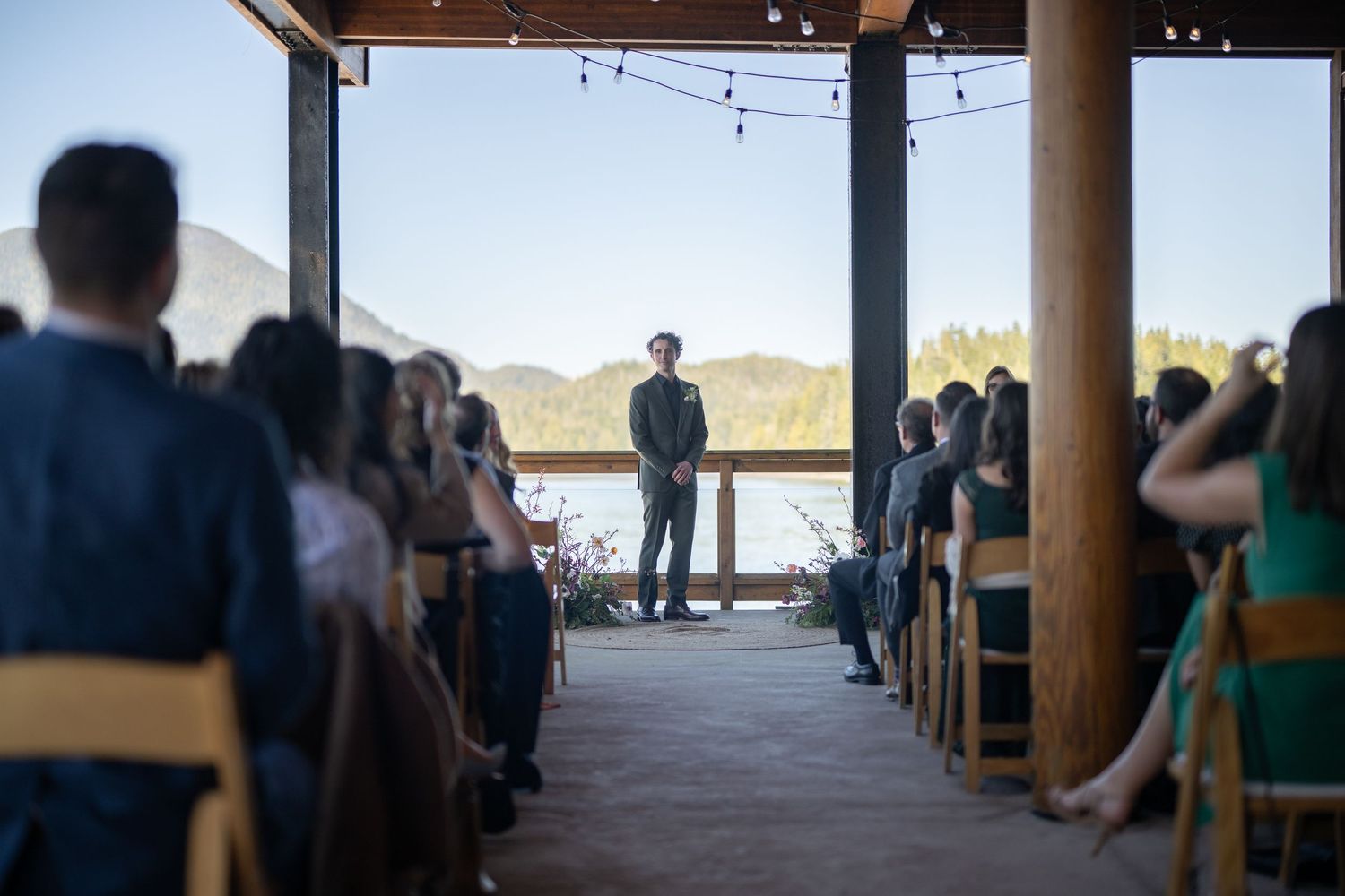 Wedding ceremony guests seated in rows at a scenic mountain venue with wooden beams overhead.
