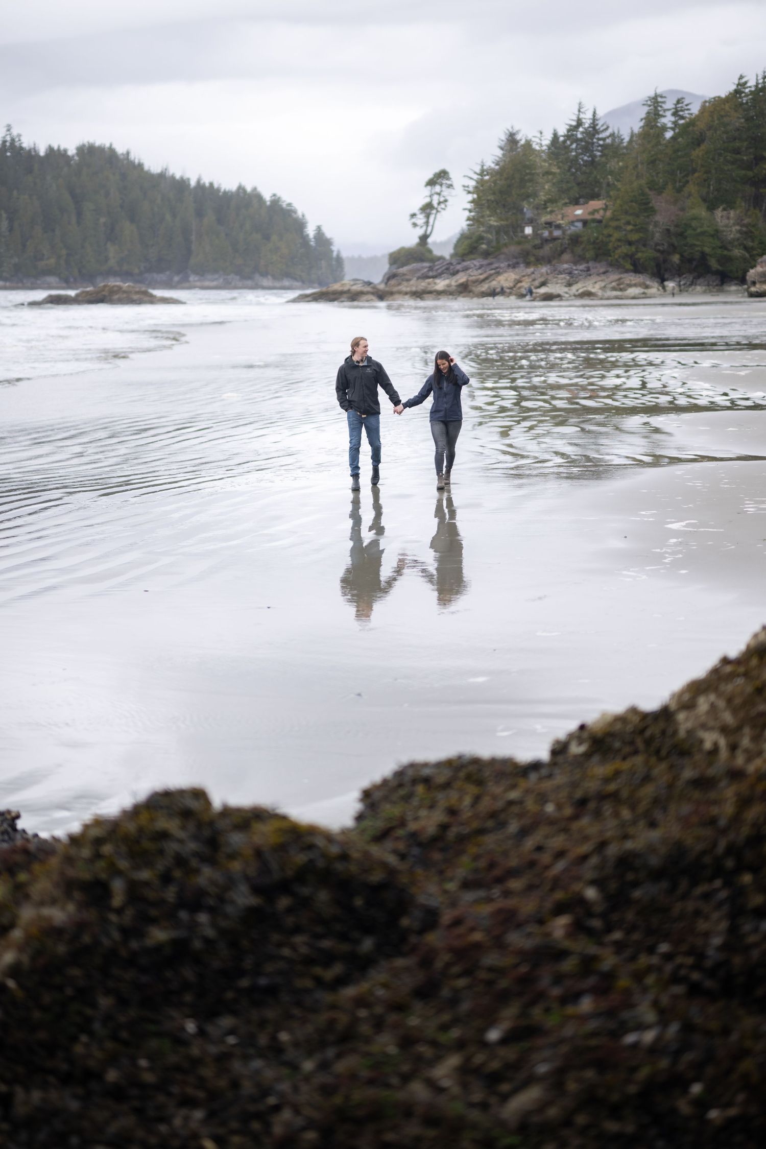 Two people walking hand in hand on a misty Pacific Northwest beach.