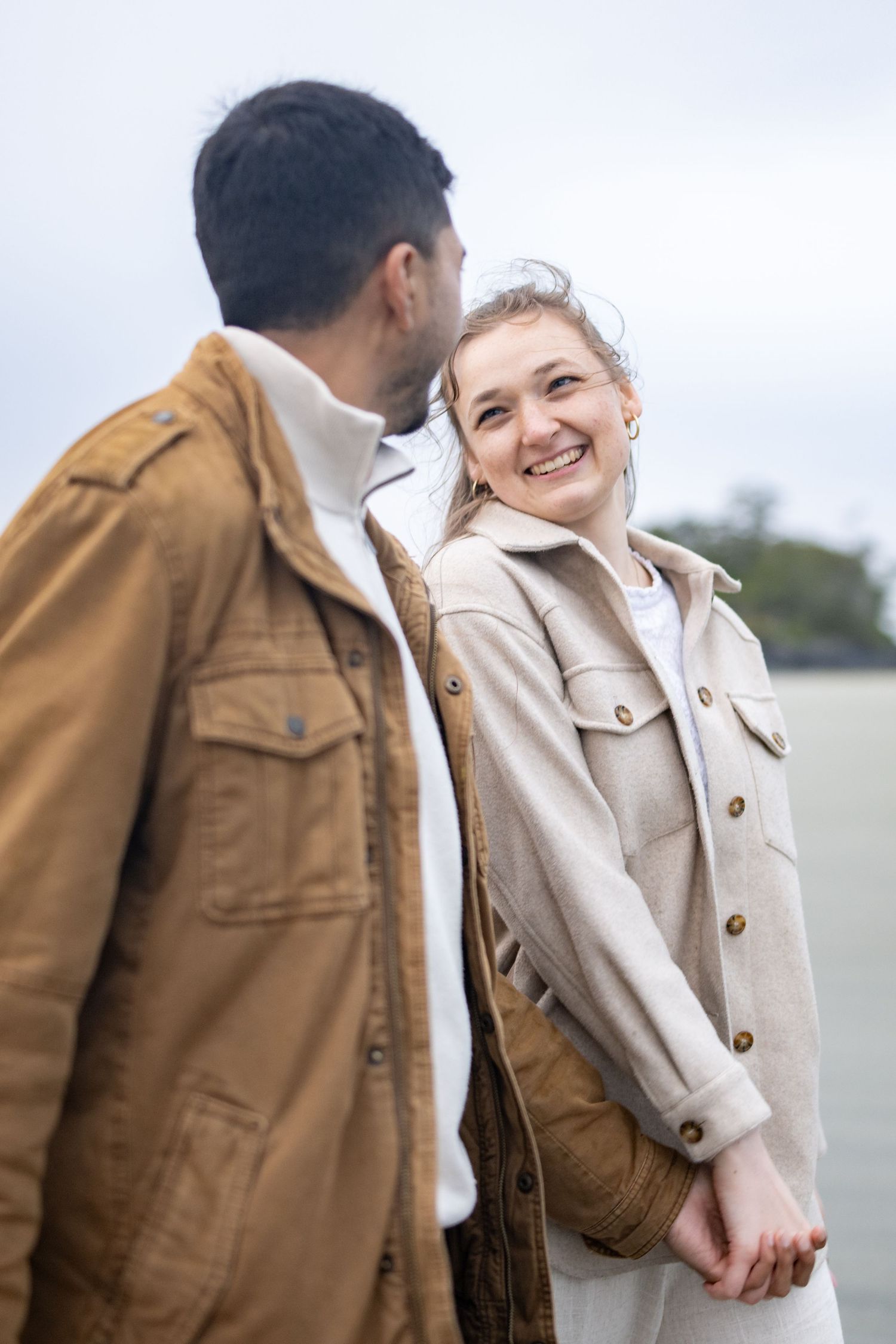 A couple wearing brown and cream jackets share intimate moments on a cloudy day.