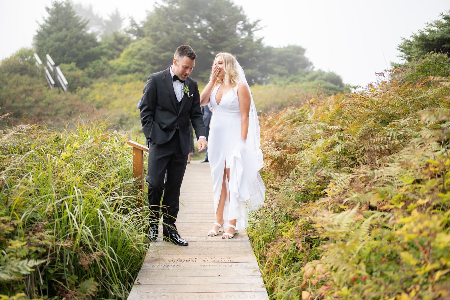 Romantic wedding photos on wooden walkway surrounded by coastal plants.