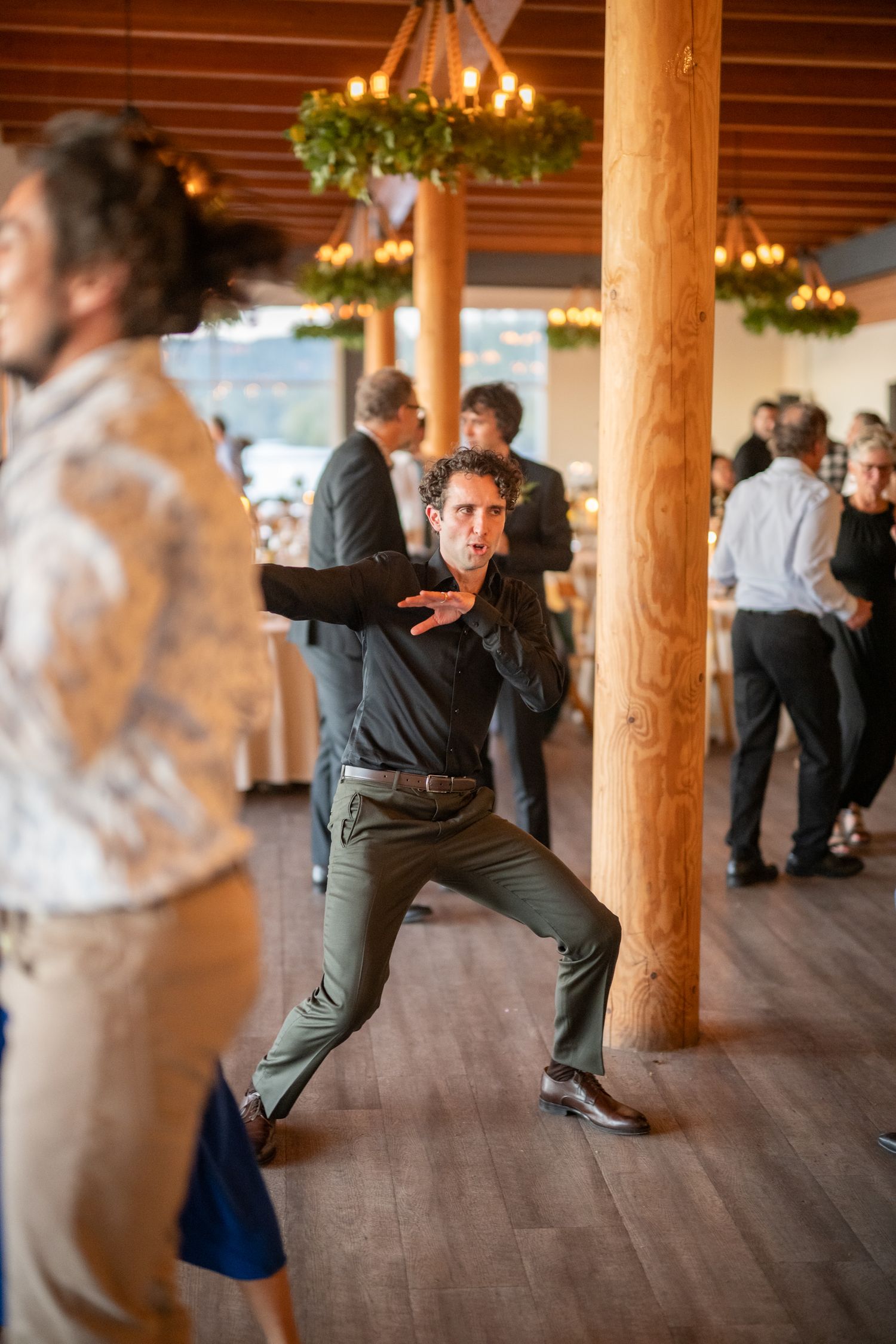 Energetic dancing on a wooden floor under rustic beams at a wedding reception.