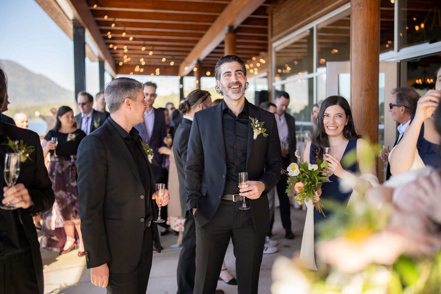 Guests mingling under wooden beams and string lights at an elegant outdoor venue.