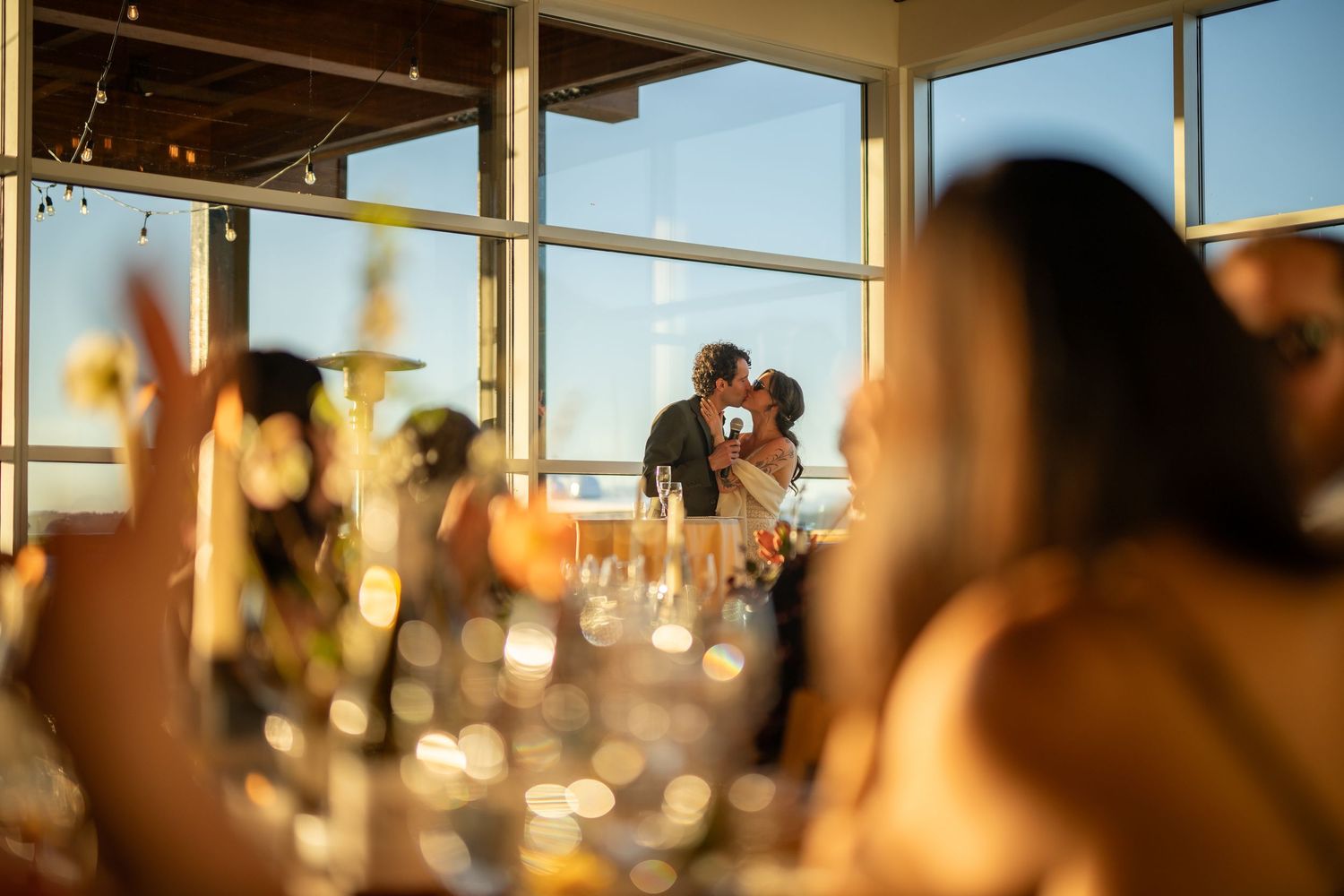 Warm sunset light fills a coastal venue through large panoramic windows.