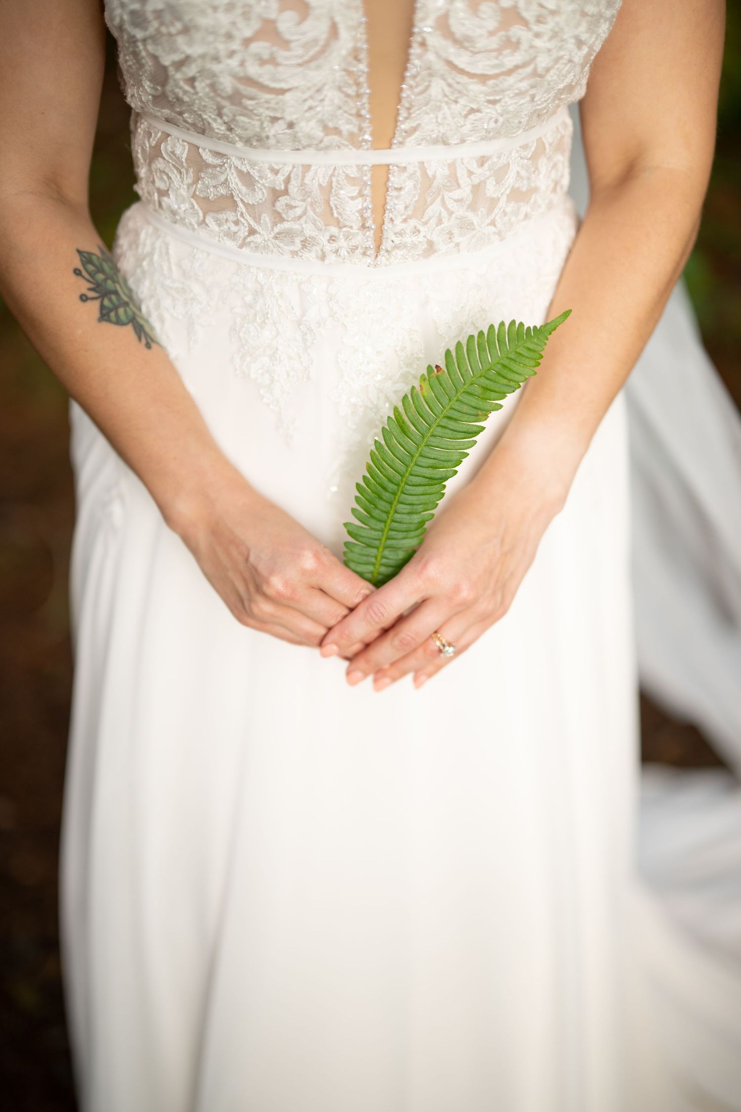 White lace wedding dress detail with green fern leaf held against bodice.
