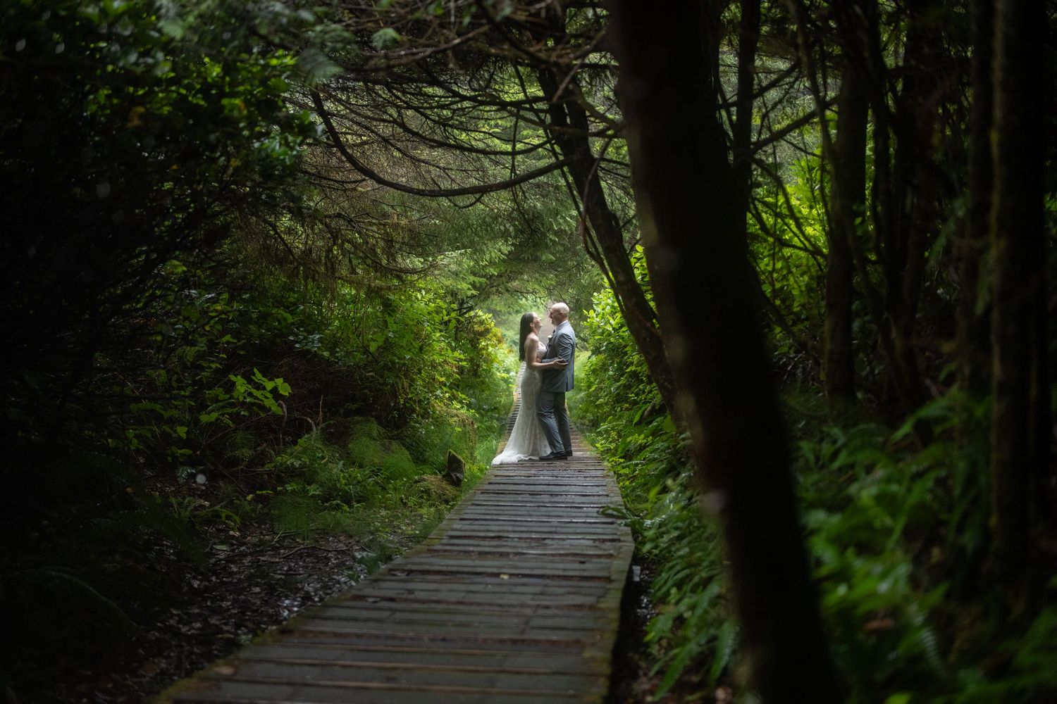 A couple walks along a wooden boardwalk path through a misty forest.