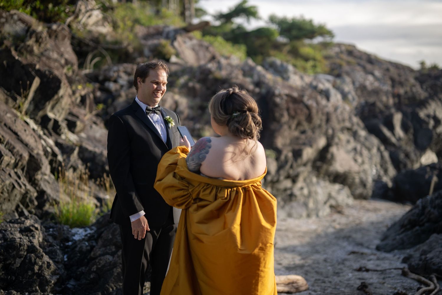A couple stands together on a rocky coastal shoreline during golden hour.