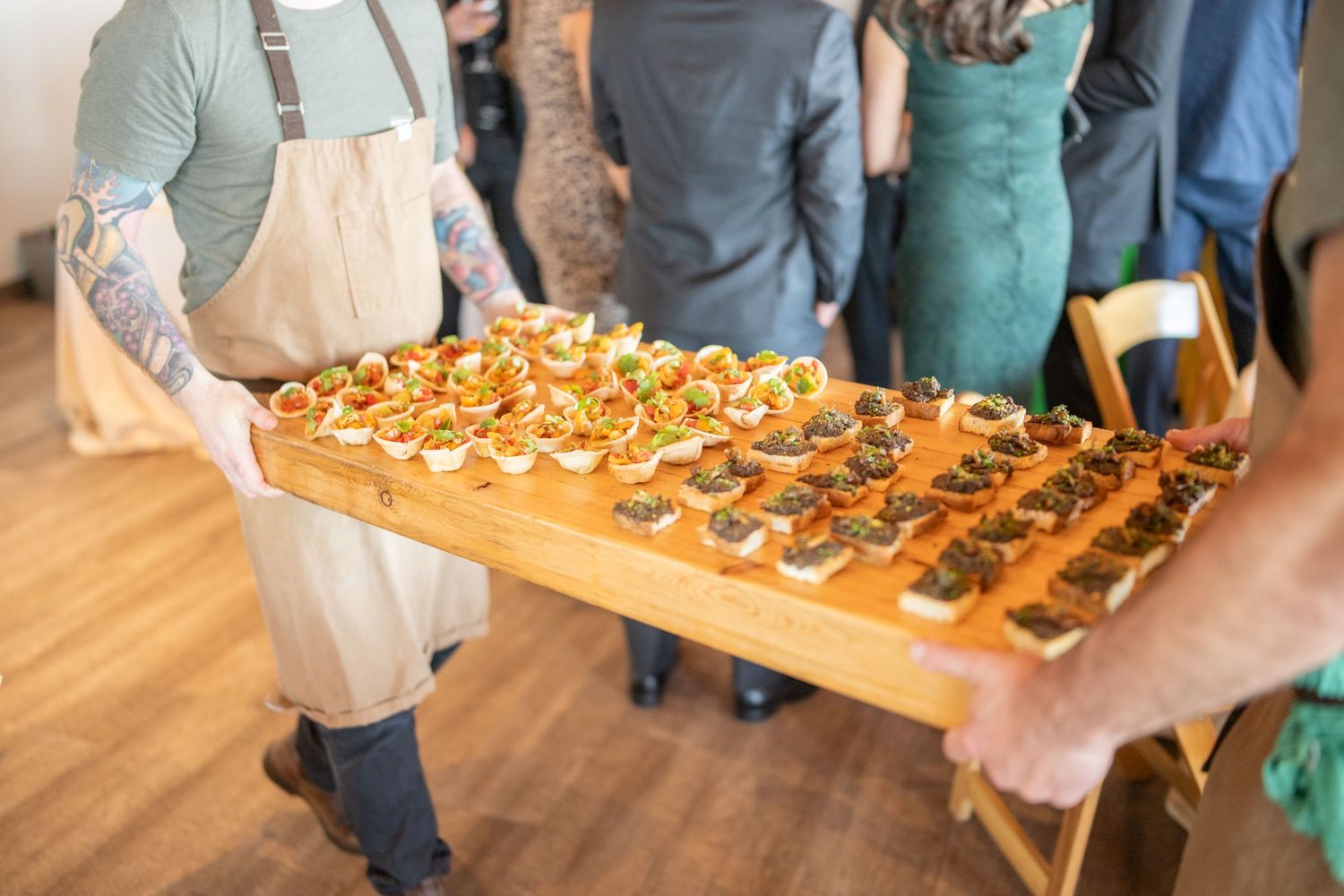 Server holding a large wooden board filled with appetizers at an elegant catering event.