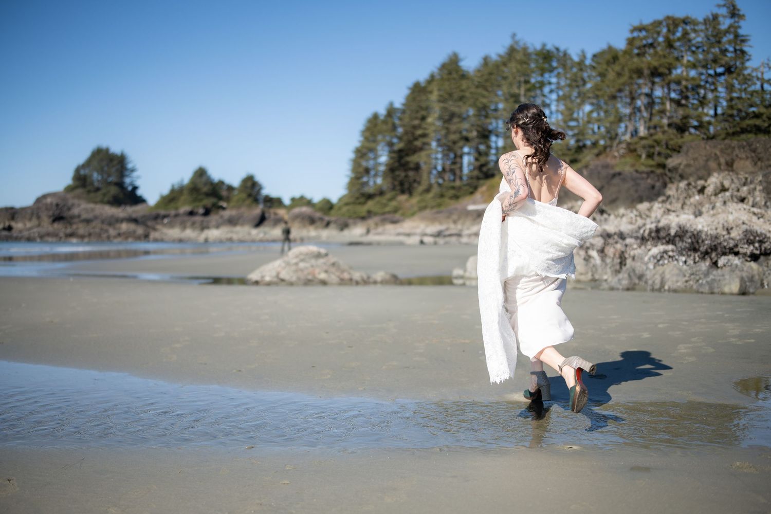 A person in a white dress walks through shallow ocean water on a scenic beach.