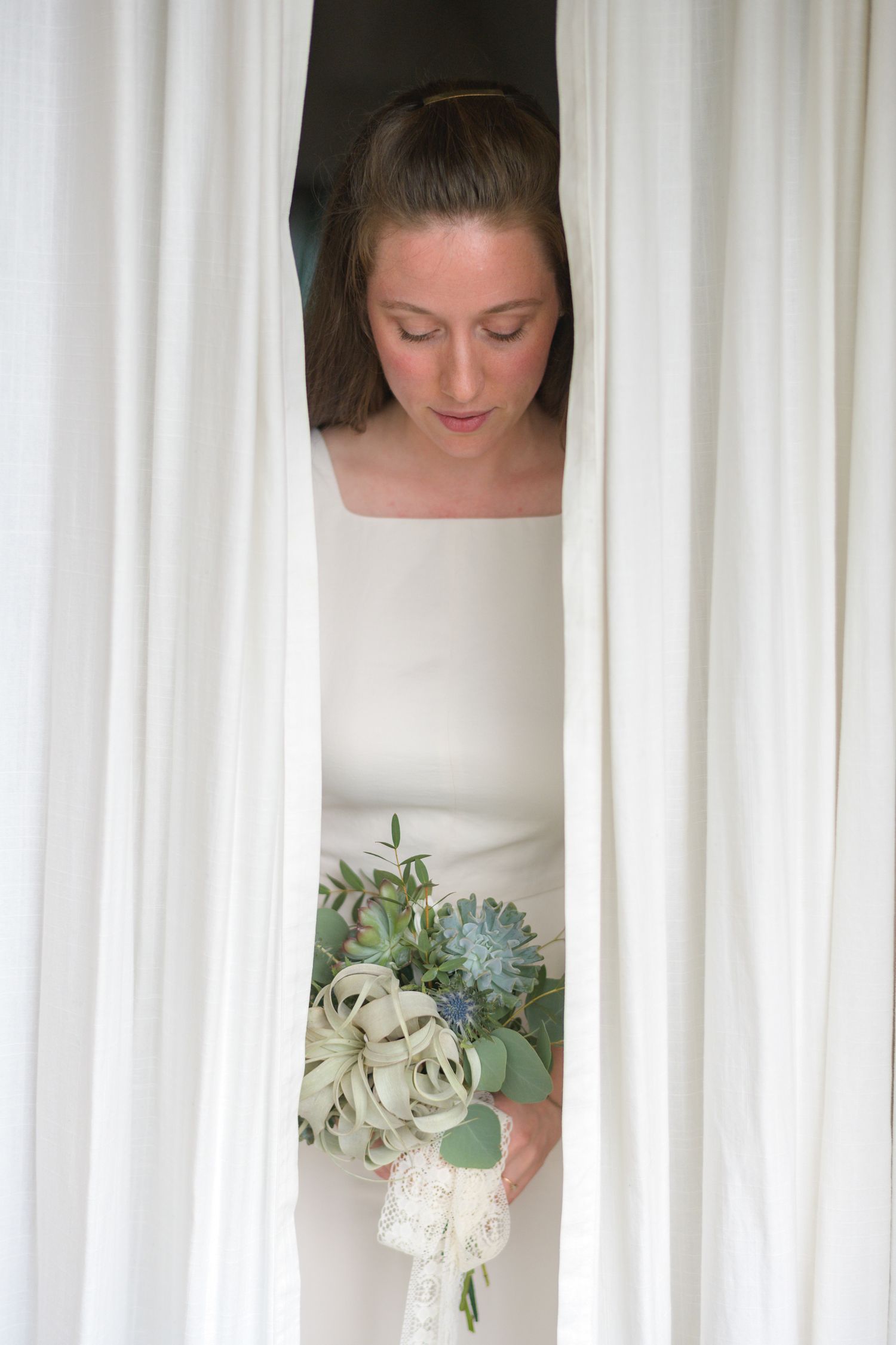 Elegant white wedding bouquet with succulents and greenery against a light curtain background.