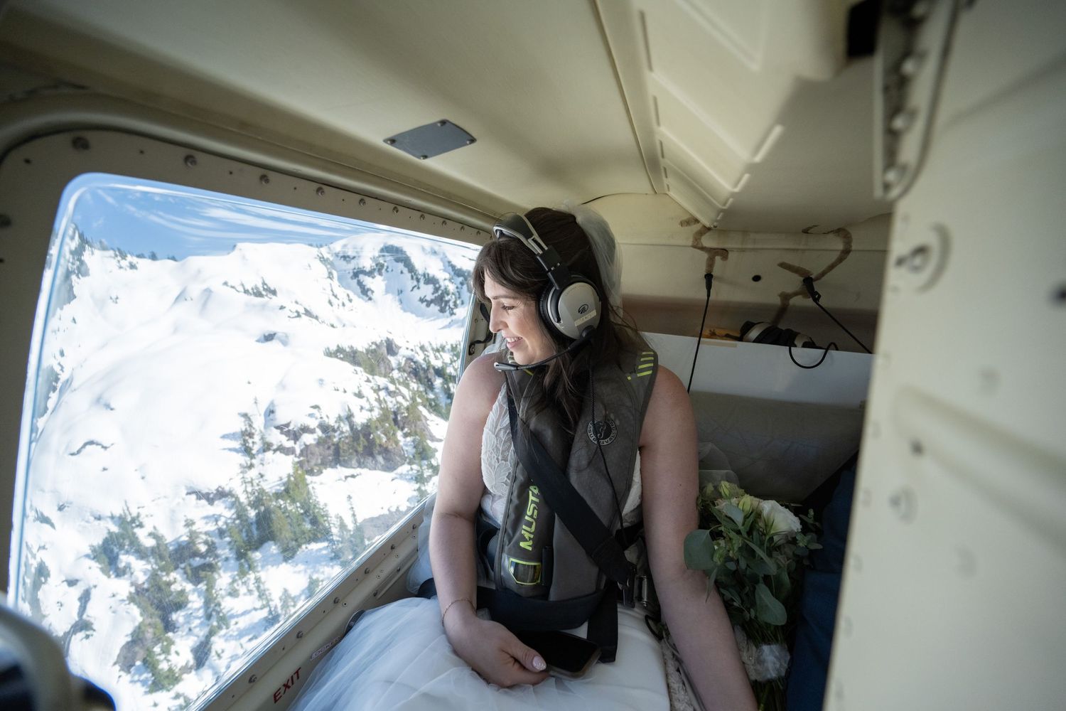 Helicopter passengers looking out windows at mountain landscape below.