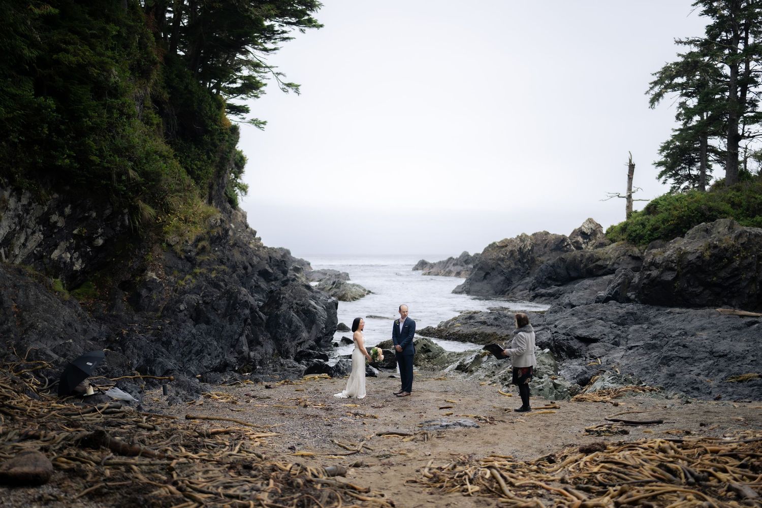 Couple exchanges vows during a private beach ceremony with rugged coastline in the background.