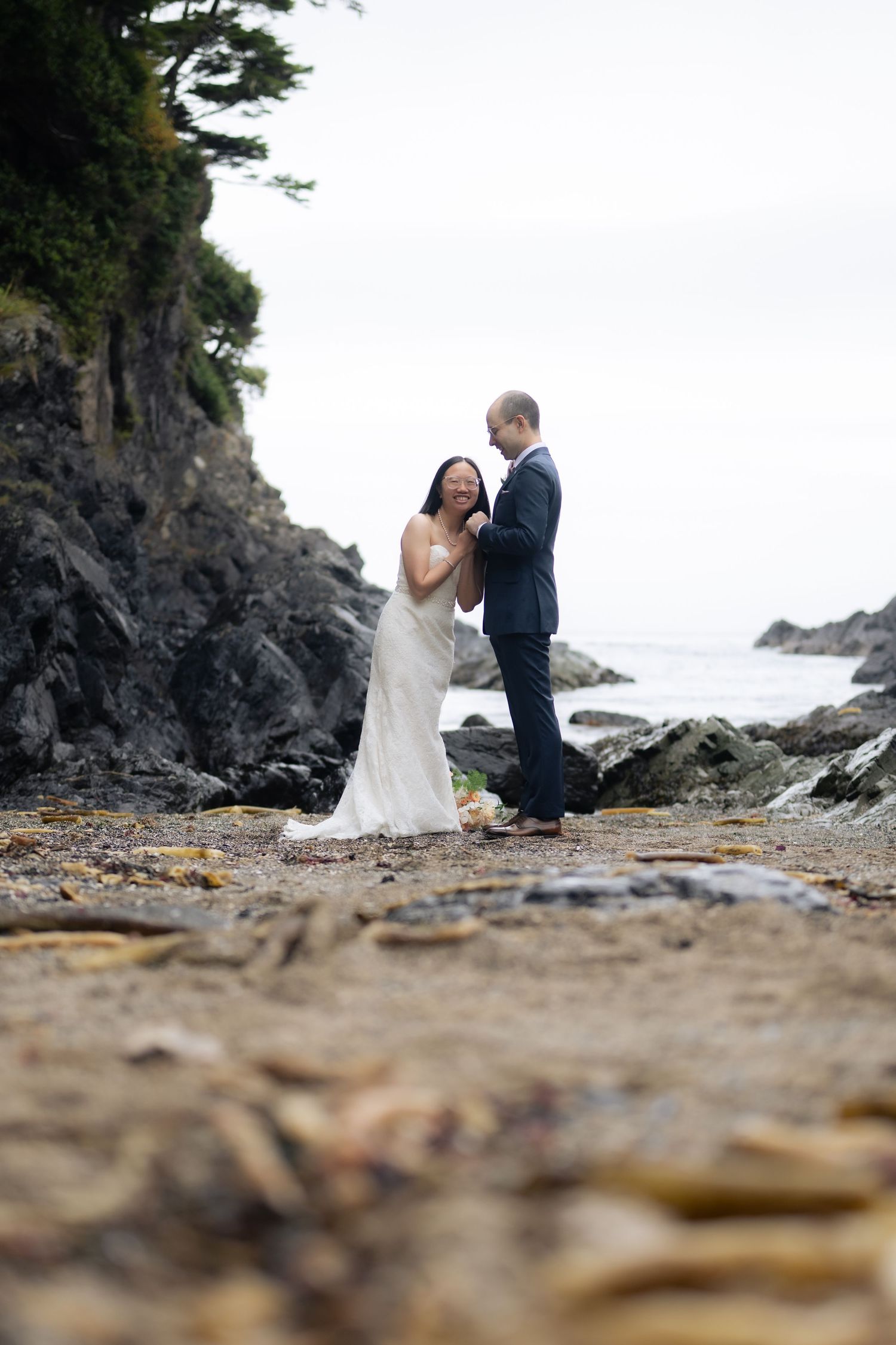 A romantic wedding ceremony unfolds on a rocky beach with dramatic coastal cliffs in the distance.