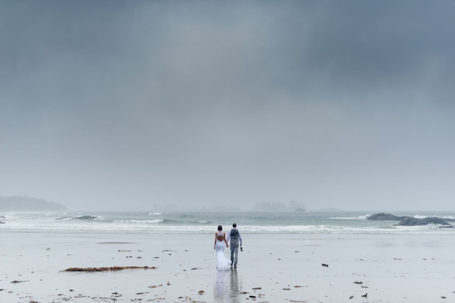 Distant view of a couple walking along a foggy beach shoreline.
