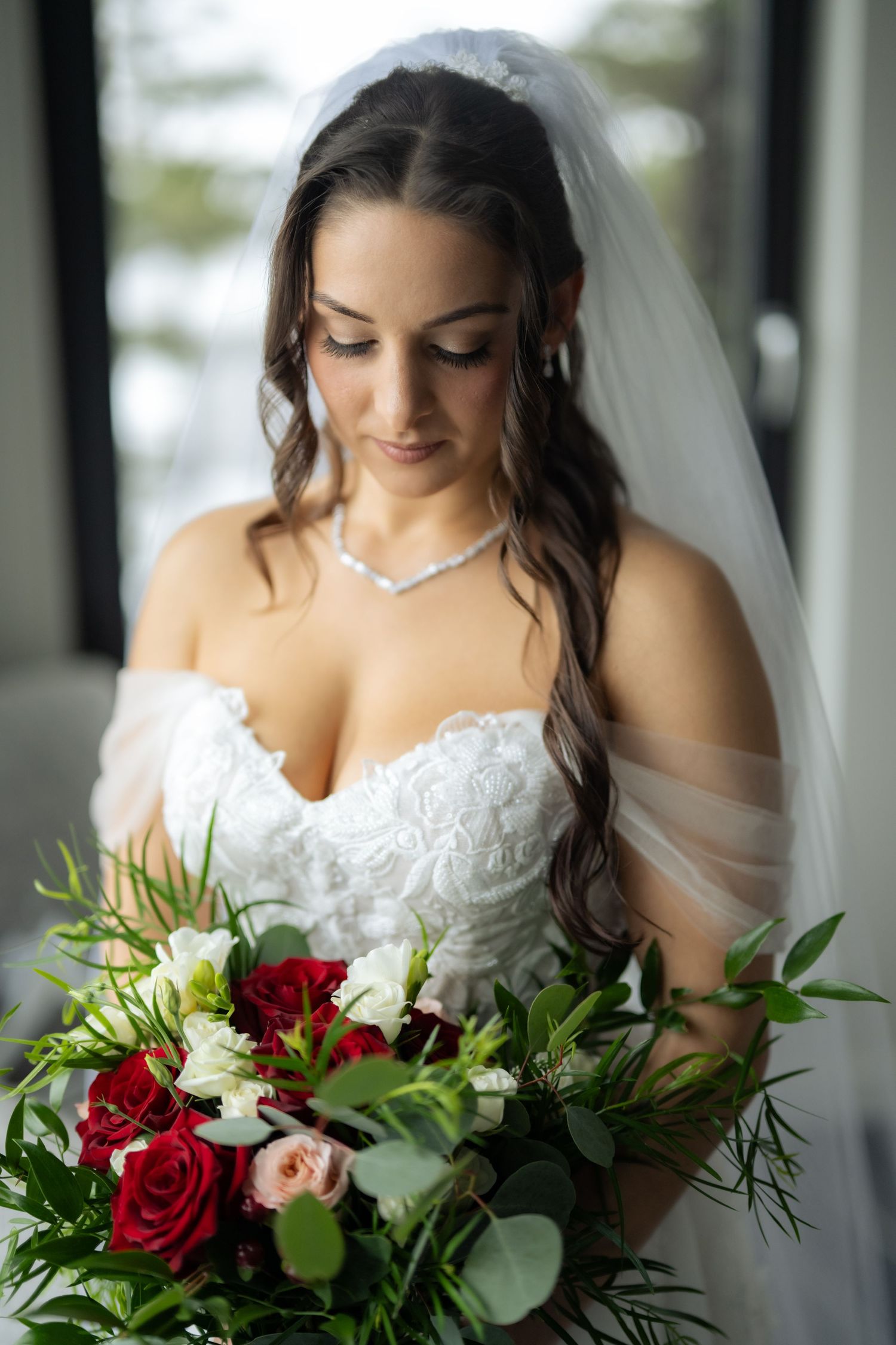 Bridal bouquet featuring deep red roses and white flowers with green foliage.