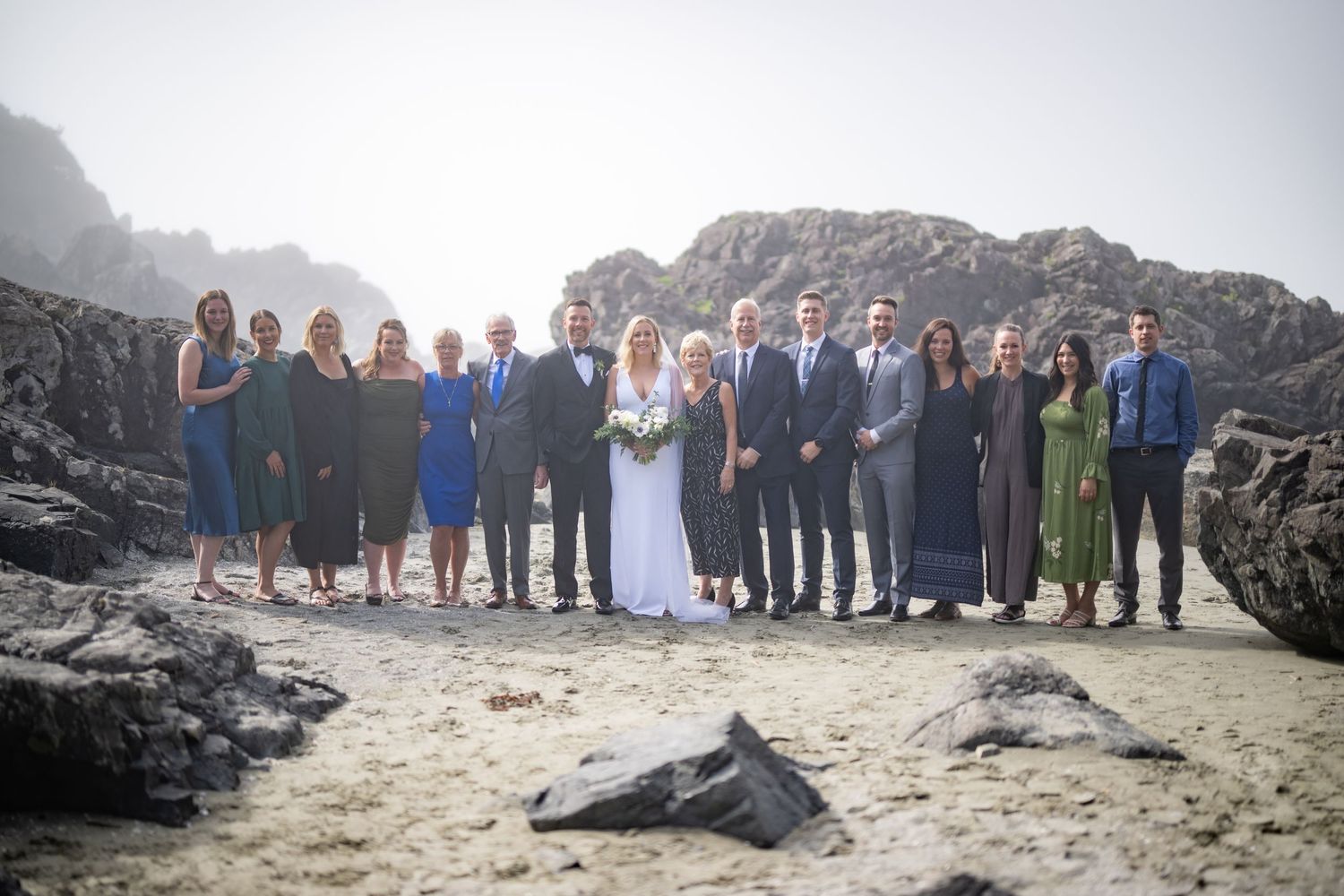 Wedding group photo with entire party lined up on scenic rocky beach.