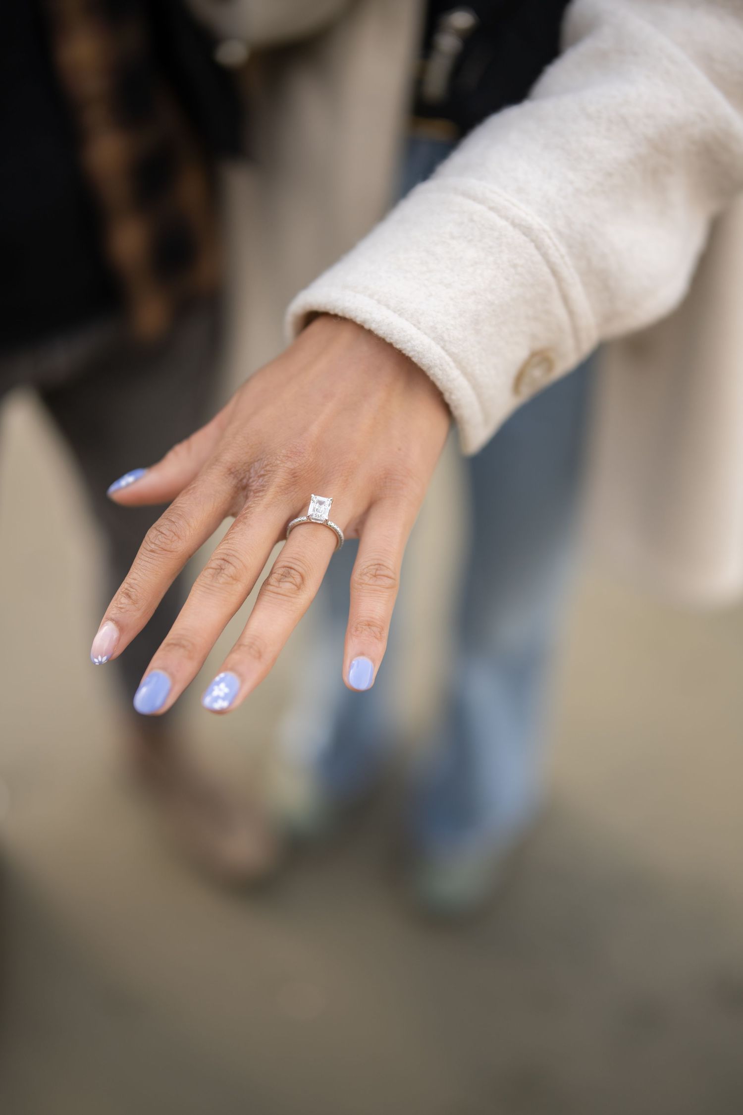 Hand with light blue ombre nails displaying a sparkling diamond engagement ring.