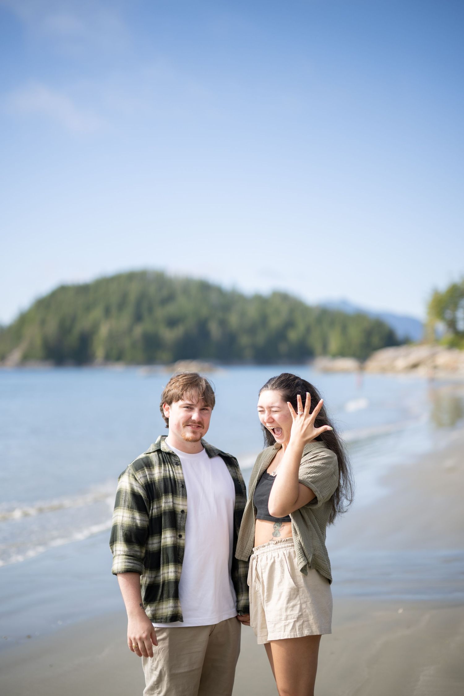 Two people share joyful laughter together on a sunny beach with mountain views.