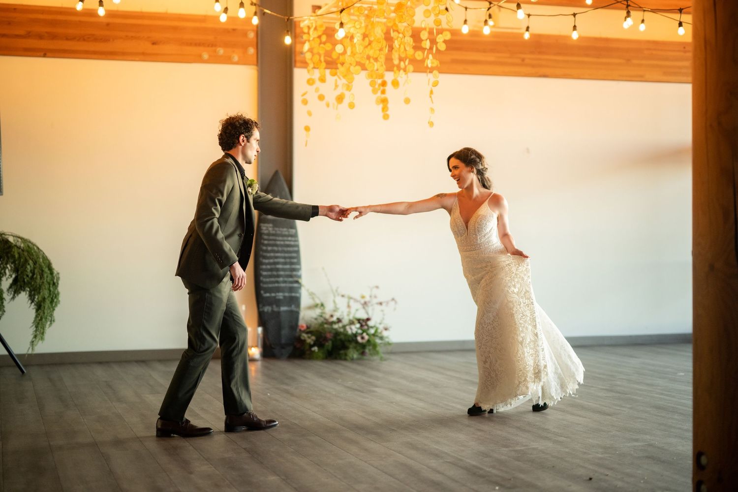 Couple dancing in elegant reception venue decorated with warm lighting and wooden accents.