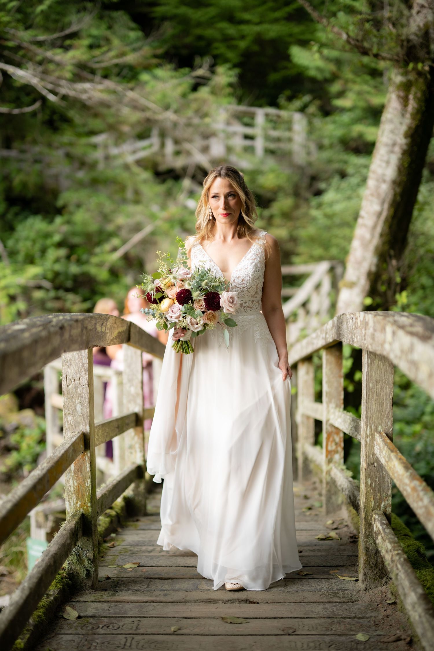 A white lace wedding dress flows elegantly across a rustic wooden bridge in a forest setting.