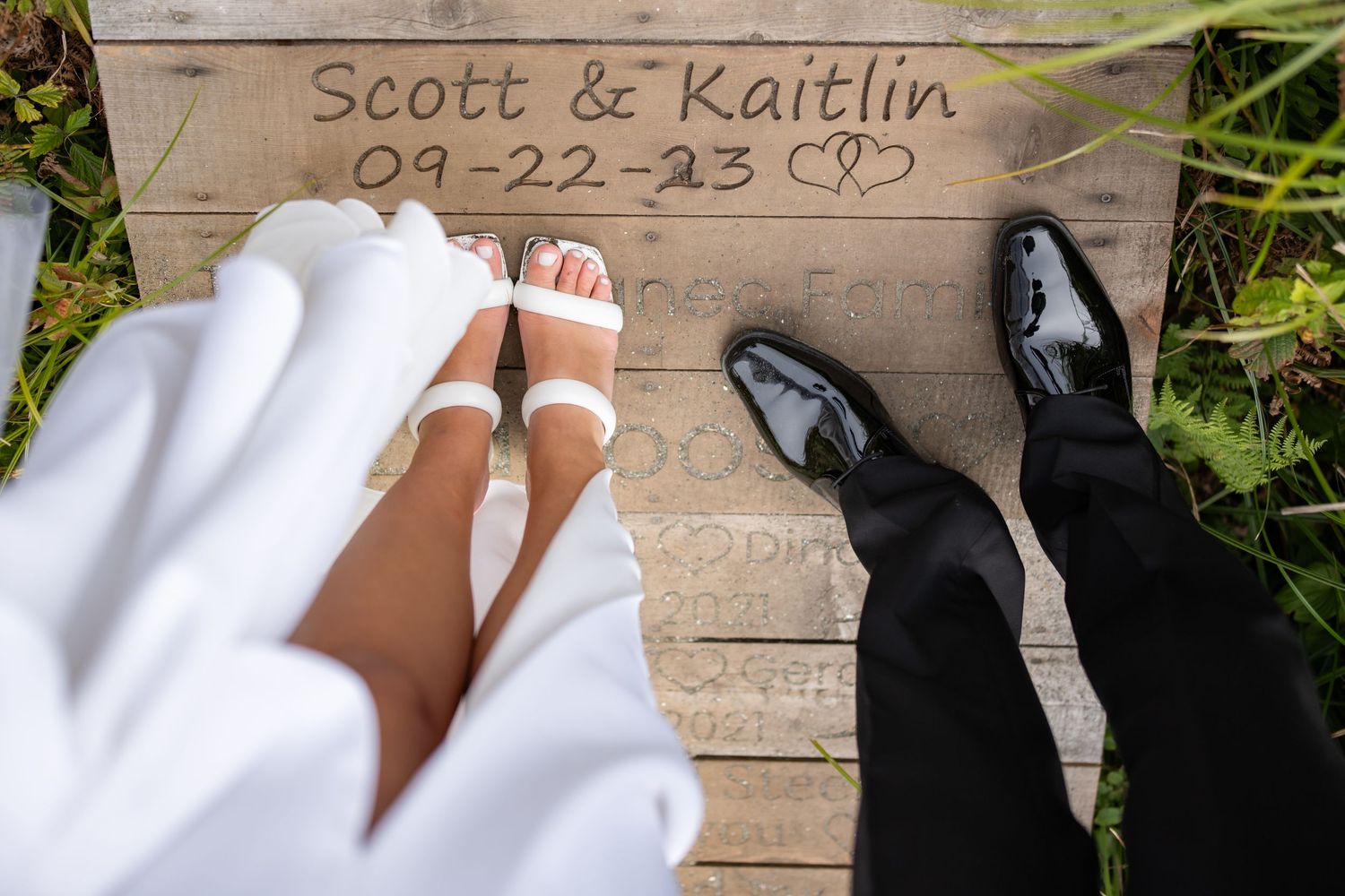 Names and date written on wooden boardwalk planks with formal shoes visible.