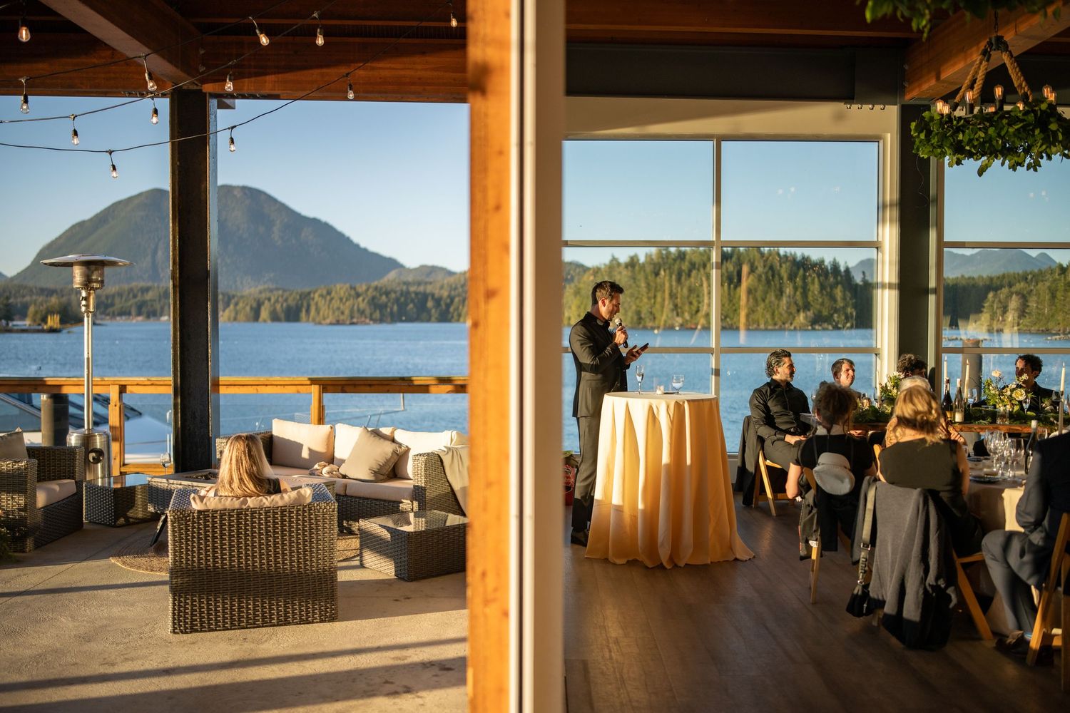 String lights illuminate a modern waterfront venue with scenic mountain views at dusk.