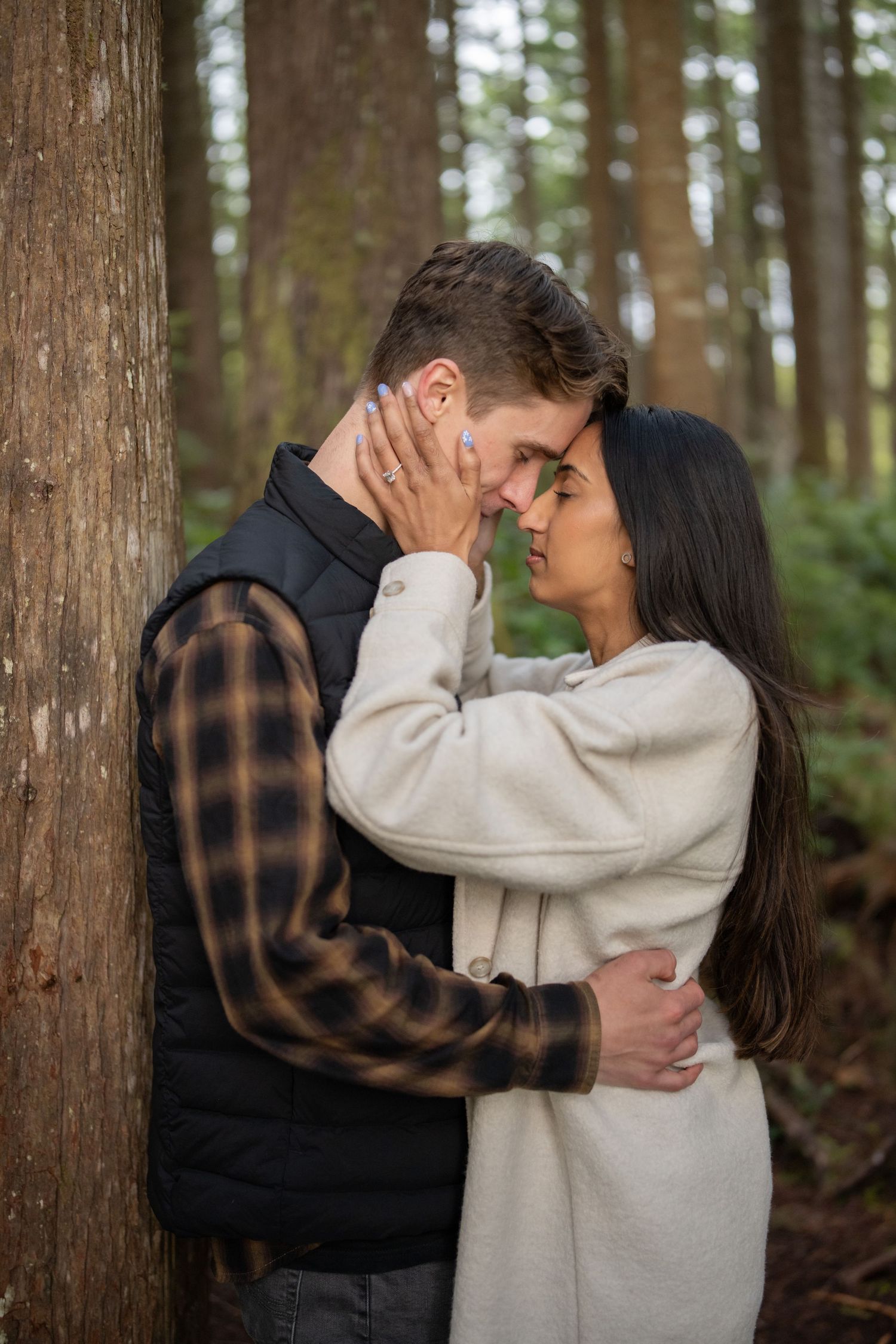 Intimate forest portrait showing two people embracing among tall evergreen trees.