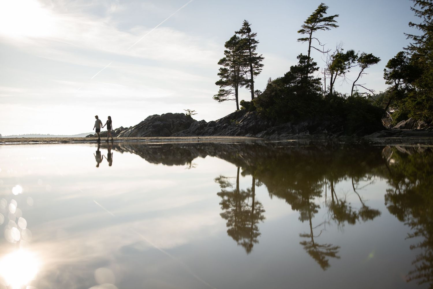 Scenic coastal landscape with evergreen trees reflected in calm waters at sunset.