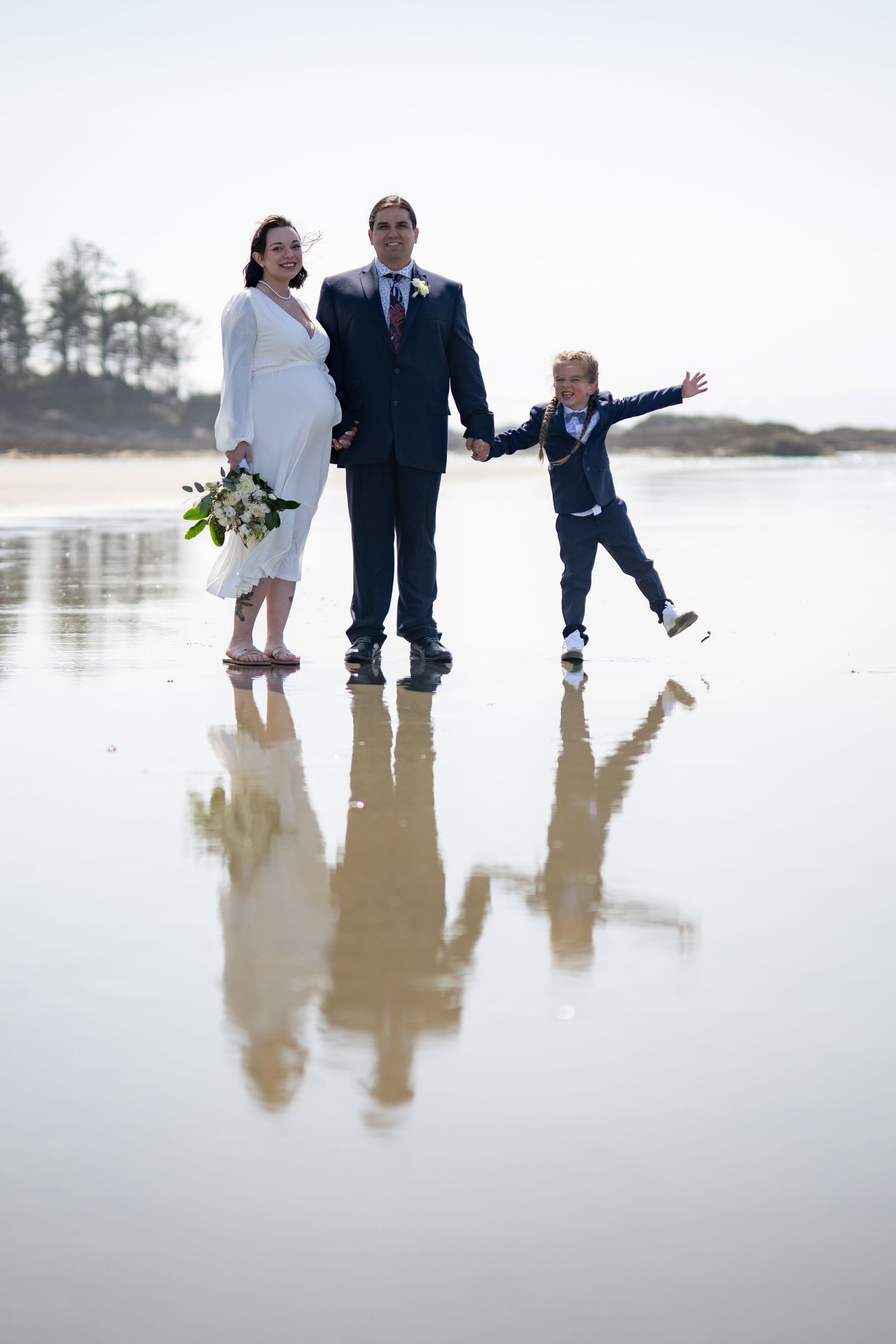 Family plays and jumps together on reflective wet beach sand.