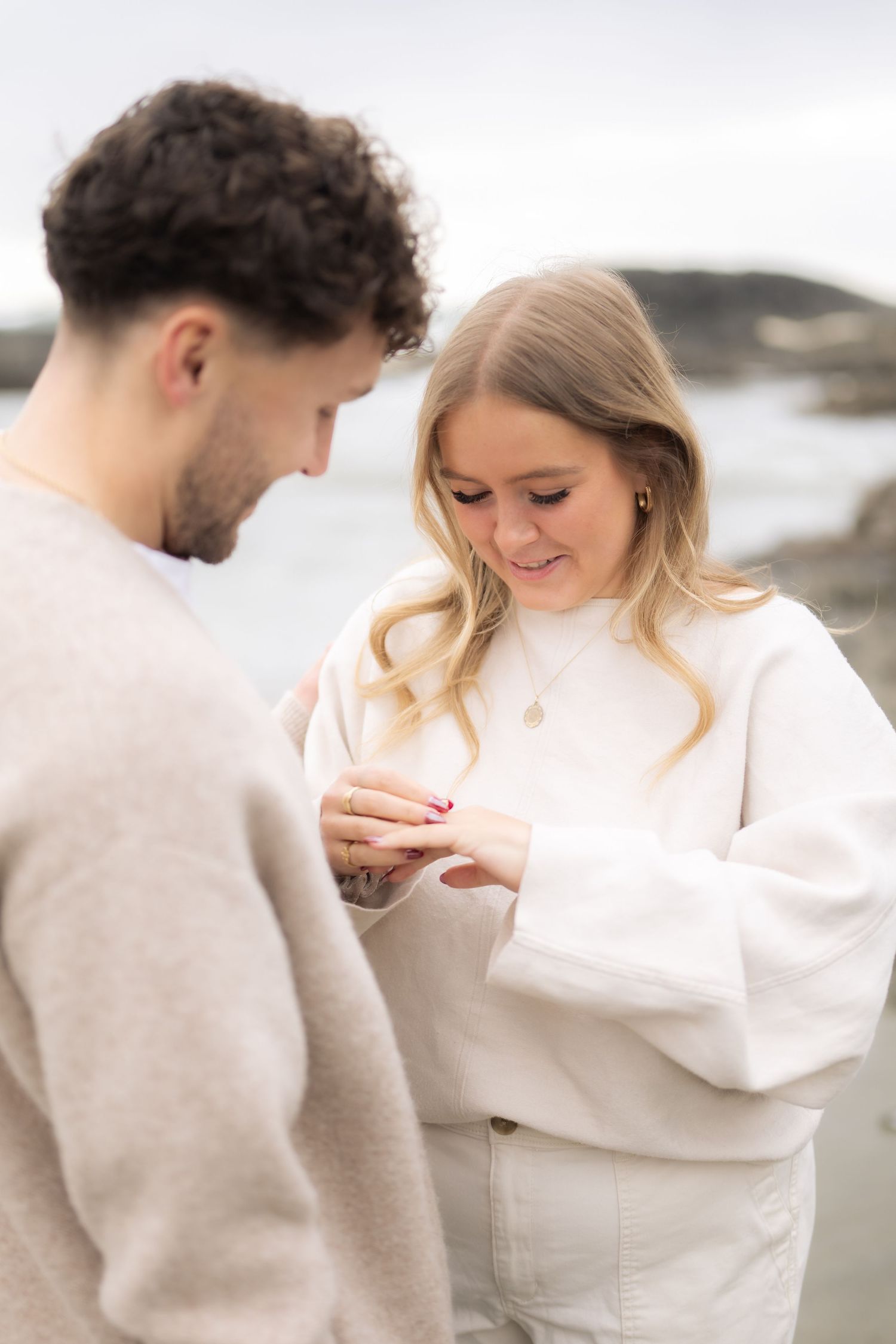 Joyful moment shared between couple as they examine ring on misty beach.