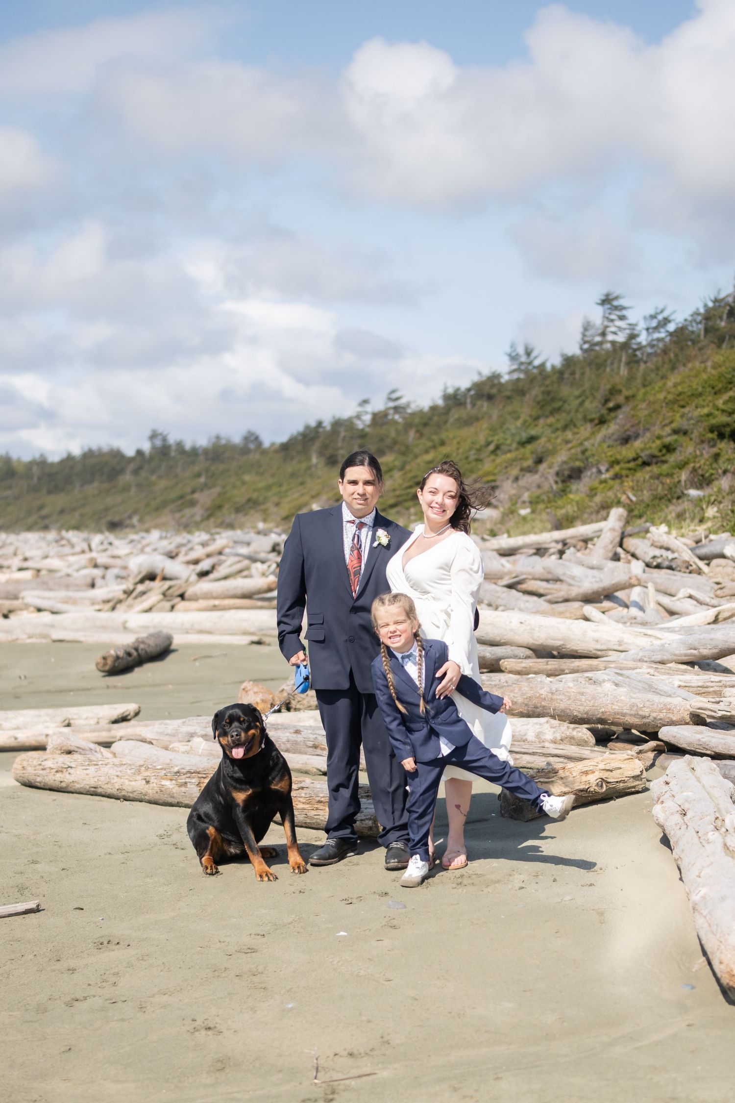 Family and dog posing near driftwood on a scenic Pacific Northwest beach.