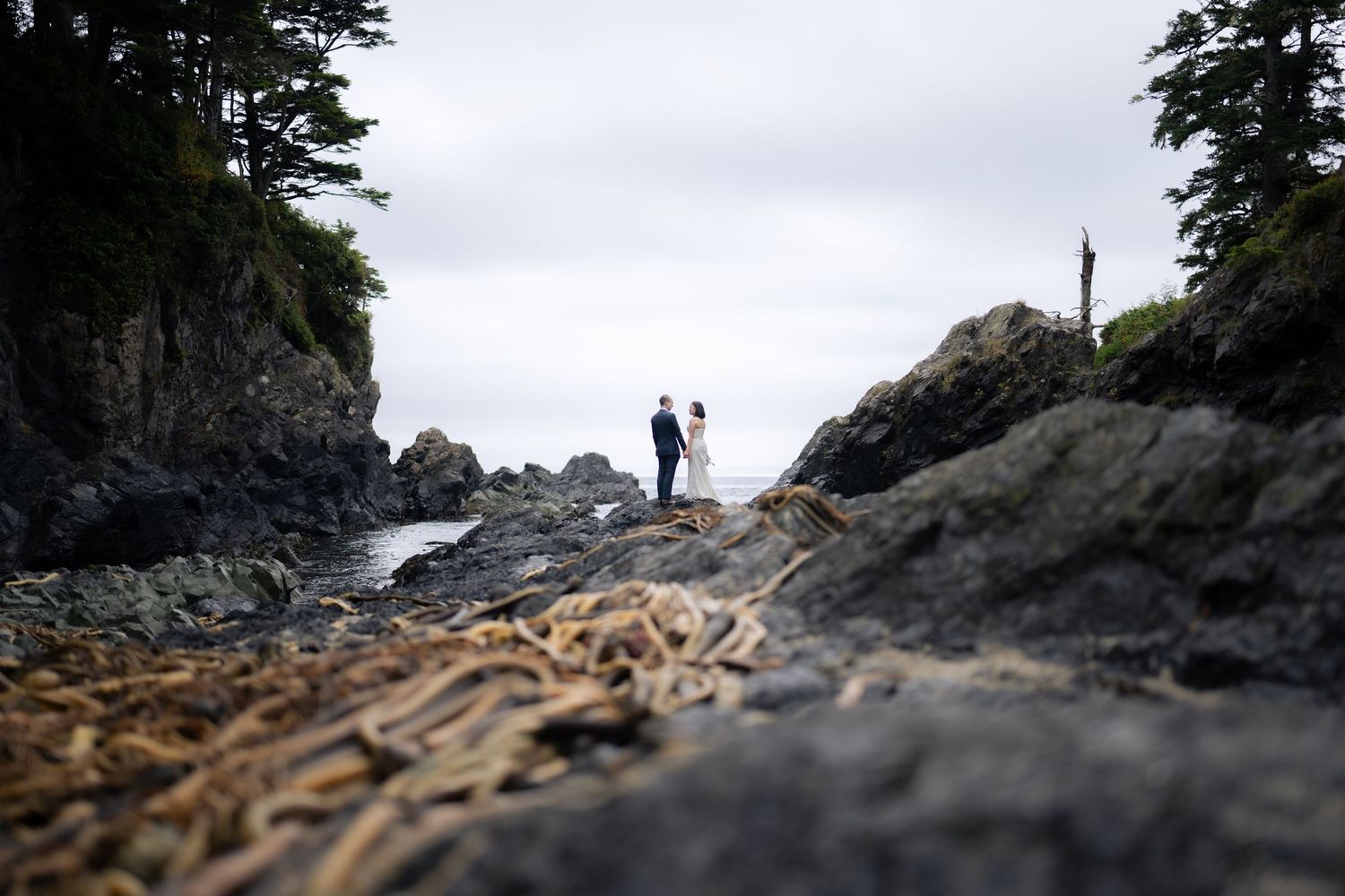 Scenic wedding photography captures distant figures against dramatic coastal rock formations.